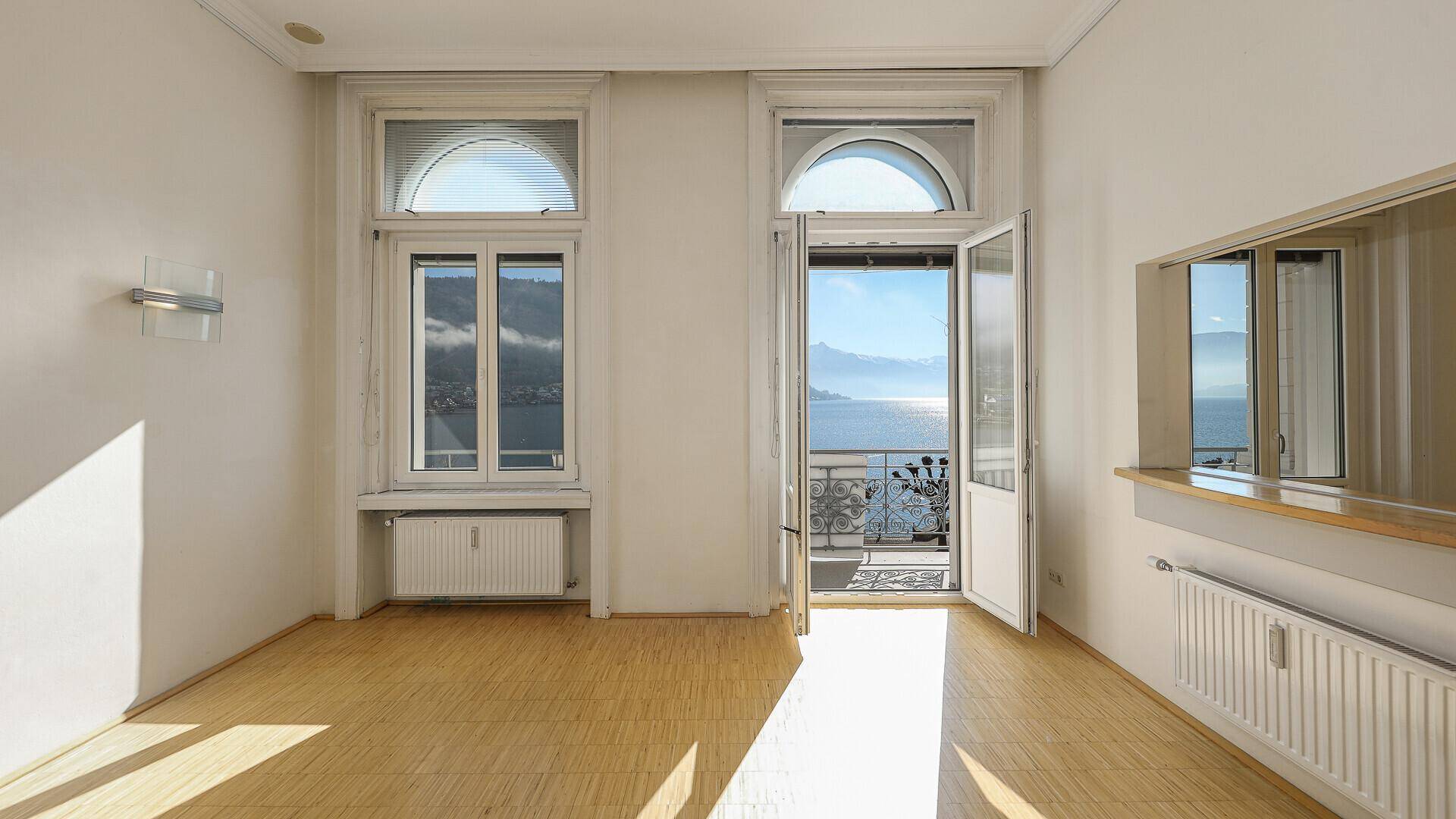 Sonniger Wohnraum mit Parkettboden und französischem Balkon mit malerischem Seeblick.