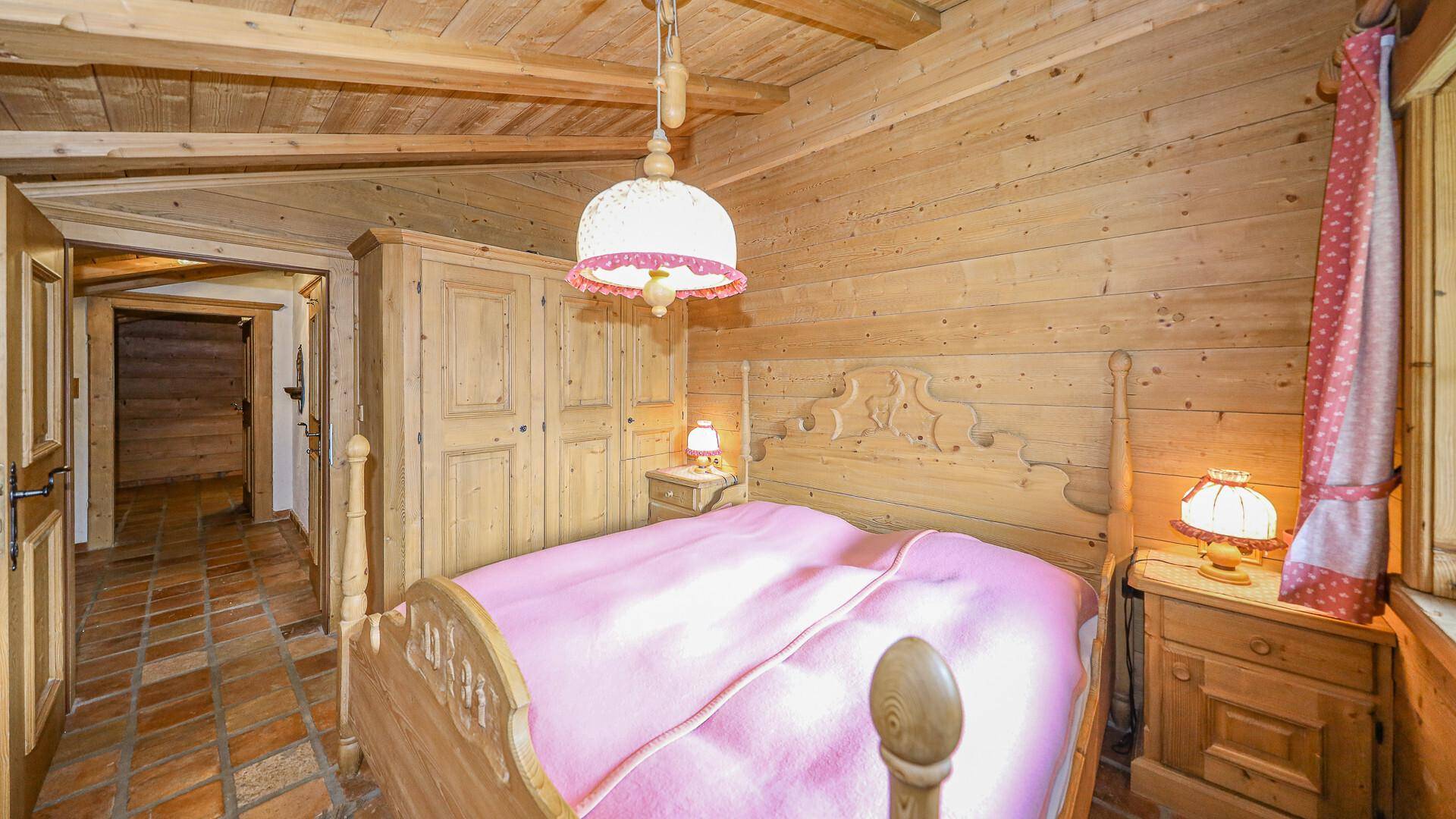 Traditionelles Schlafzimmer mit Holzvertäfelung, rustikalem Bett und Fliesenboden.
