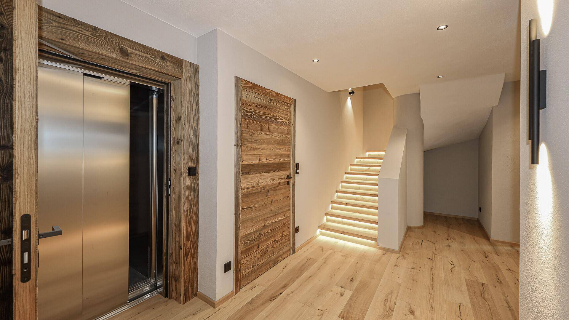 Heller Eingangsbereich mit Holzdetails, beleuchteter Treppe und modernem Aufzug.