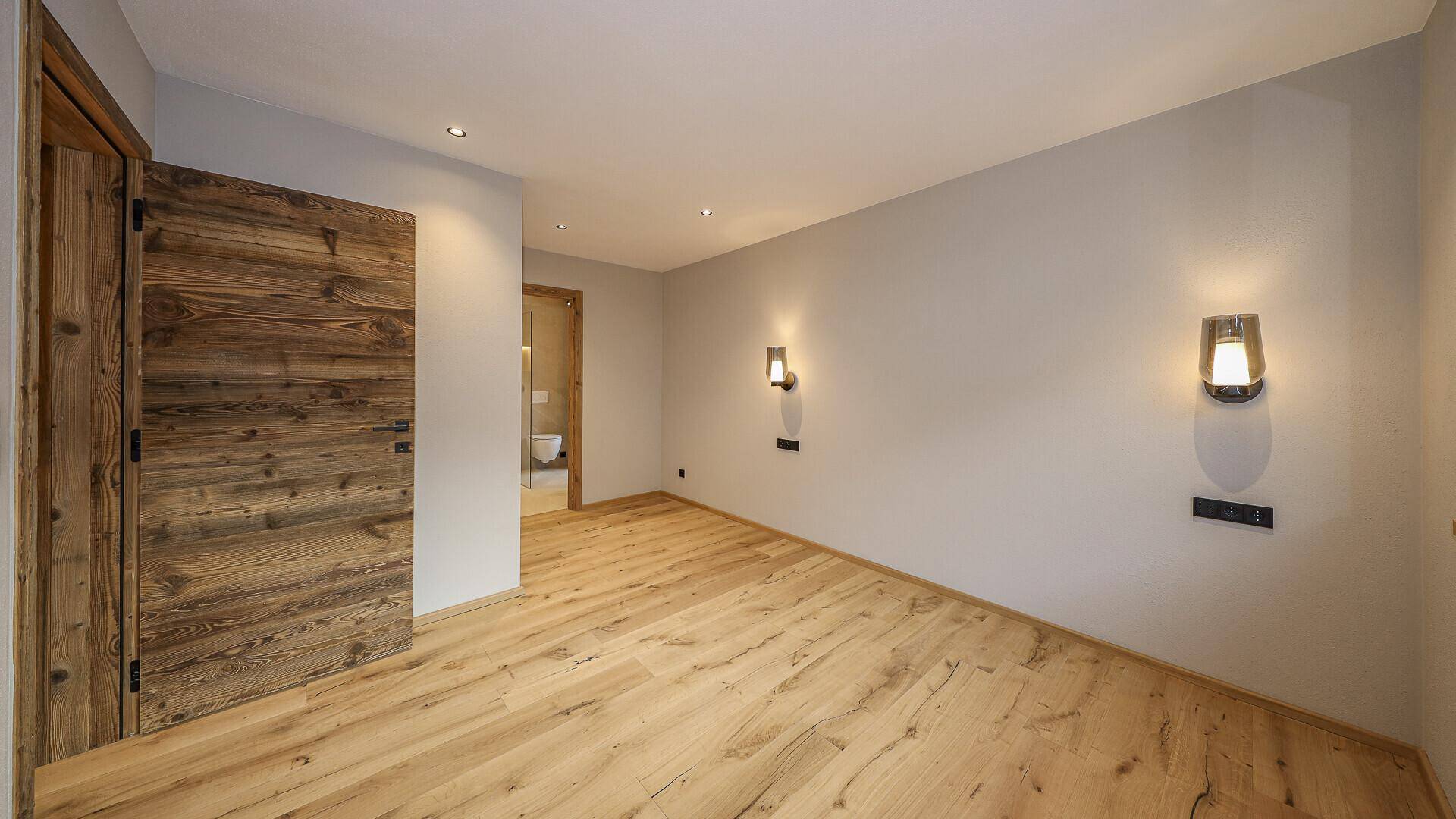Helles Schlafzimmer mit Holzboden und Holztür, bereit für individuelle Gestaltung.