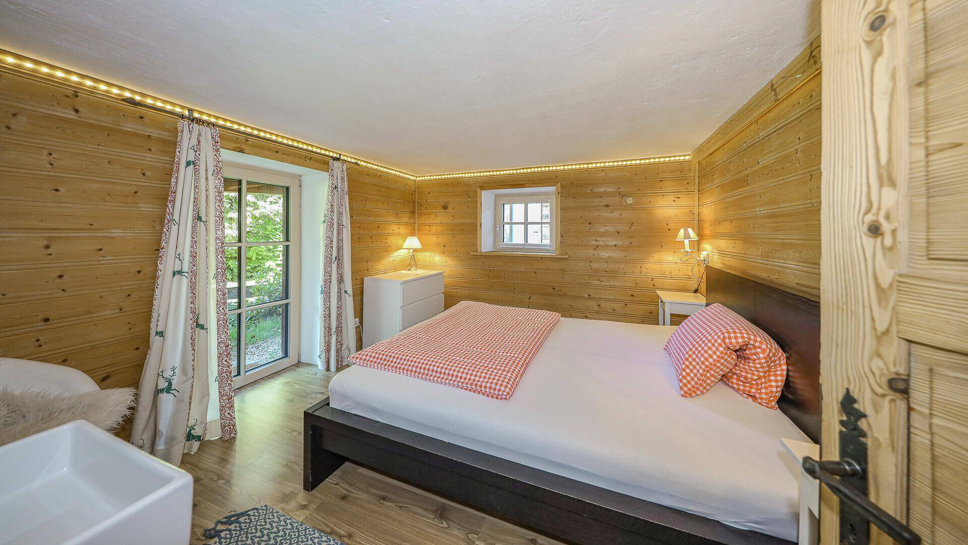 Gemütliches Schlafzimmer im alpinen Stil mit Holzvertäfelung, Doppelbett und Zugang zum Außenbereich.
