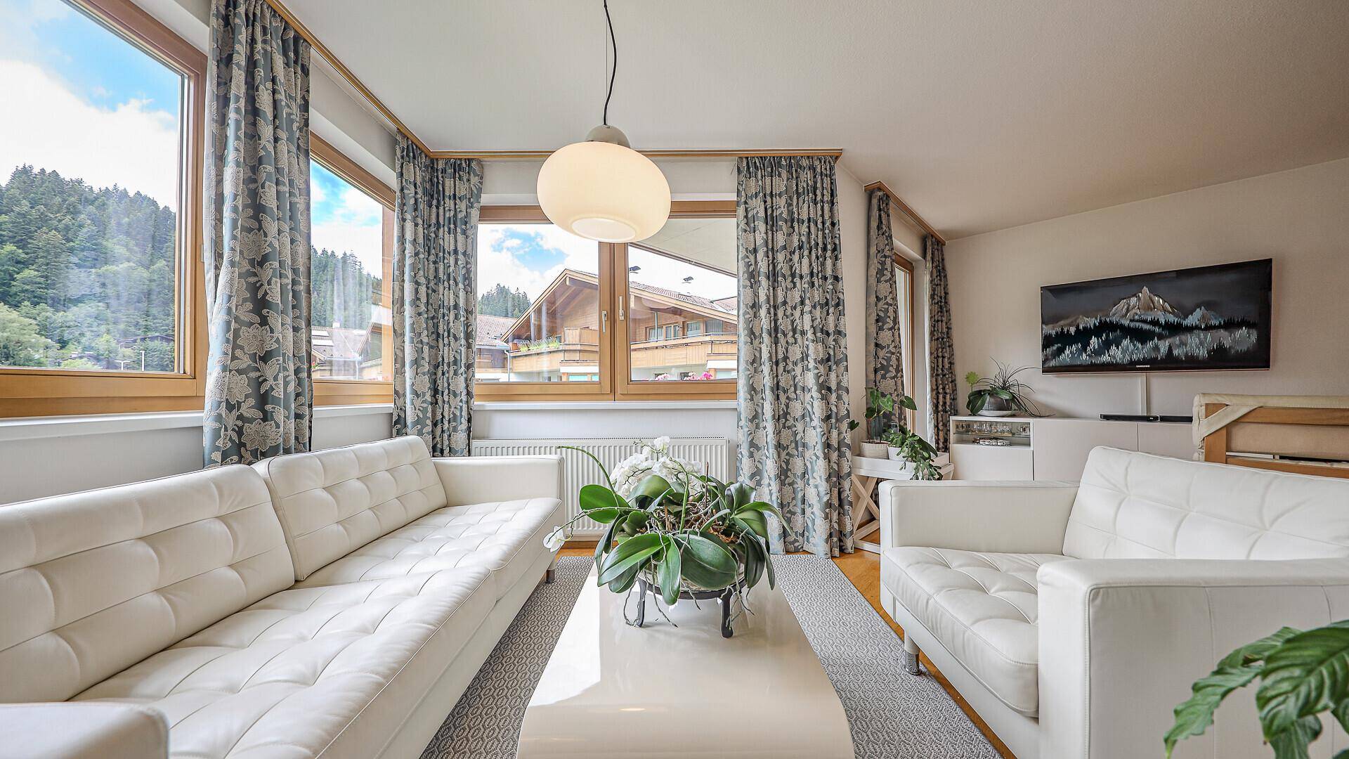 Helles Wohnzimmer mit bequemen Sofas, großen Fenstern und herrlichem Bergblick.