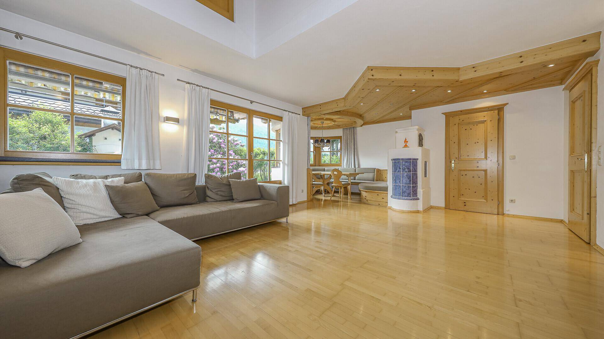 Helles Wohnzimmer mit großzügiger Couch, Holzboden und Blick ins Grüne durch große Fenster.