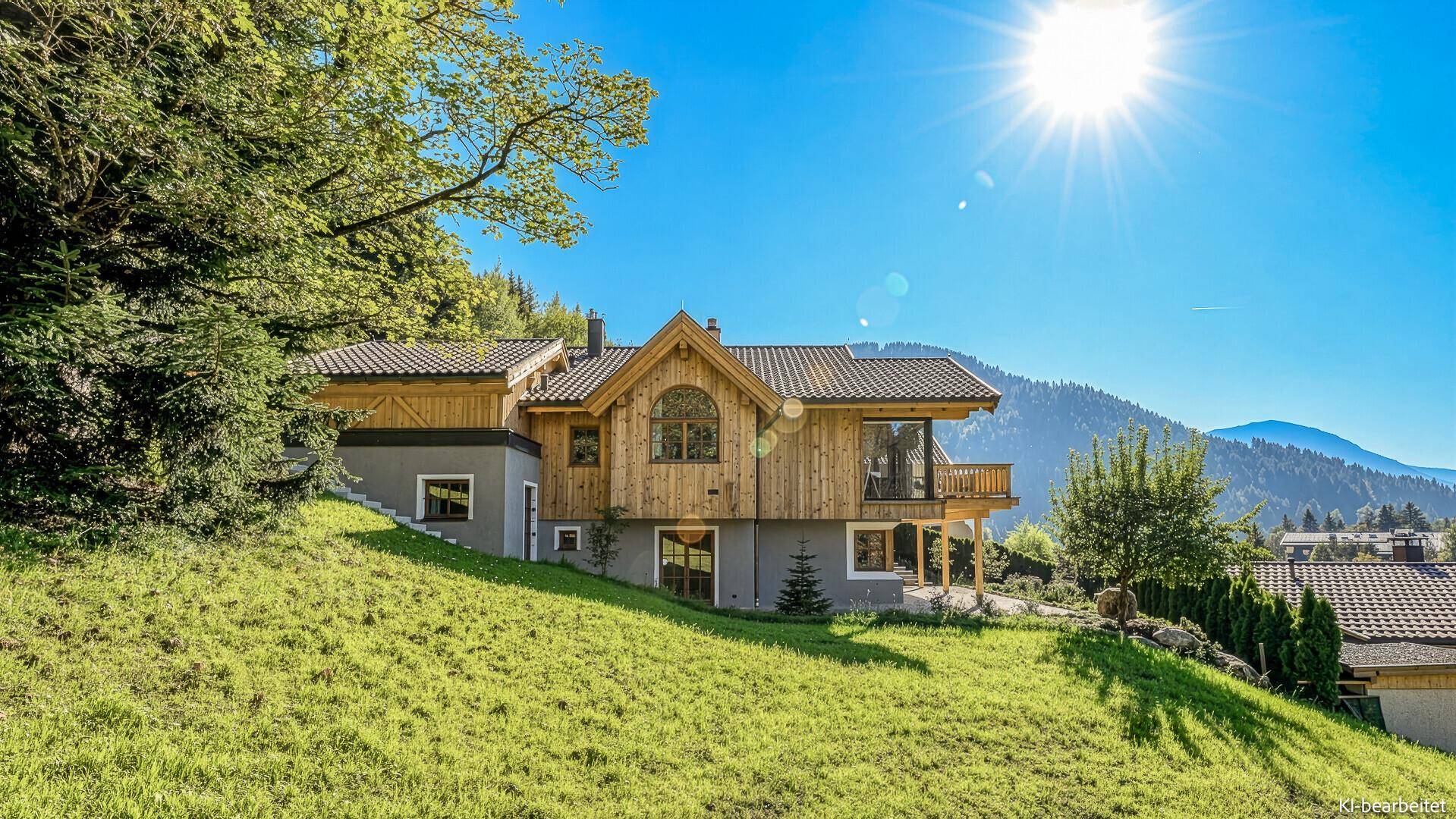 Modernes Chalet-Haus auf einem grünen Hügel mit Holzelementen und Bergblick unter strahlendem Sonnenschein.