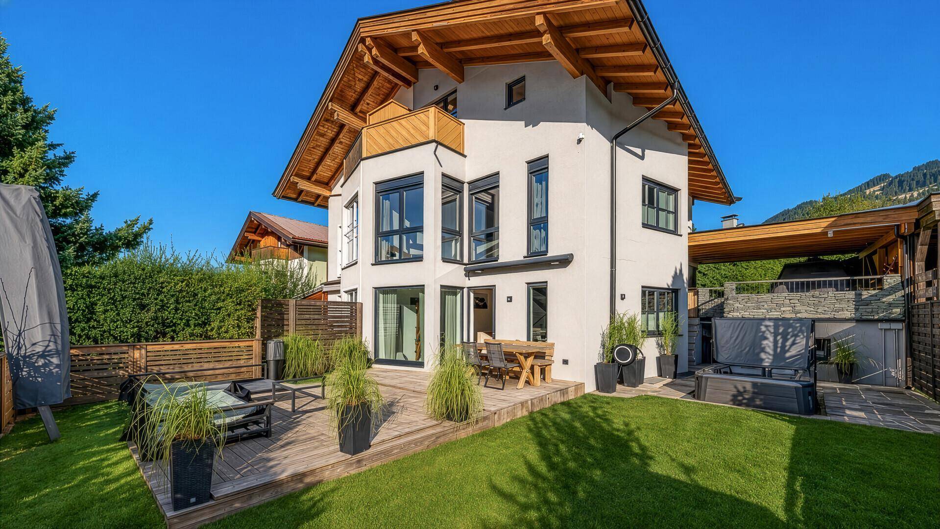 Modernes Haus mit großem Garten, Holzterrasse und integriertem Whirlpool, umgeben von viel Grün.
