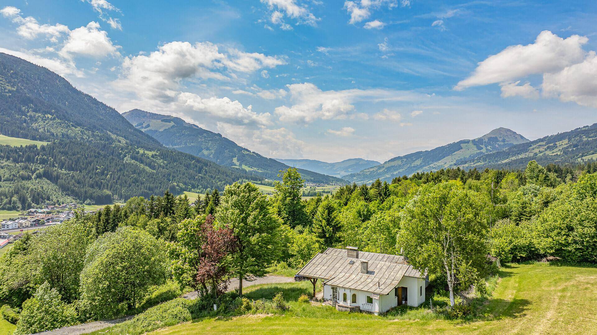 Panoramablick auf ein kleines Haus in idyllischer Berglandschaft mit weiten Wiesen.