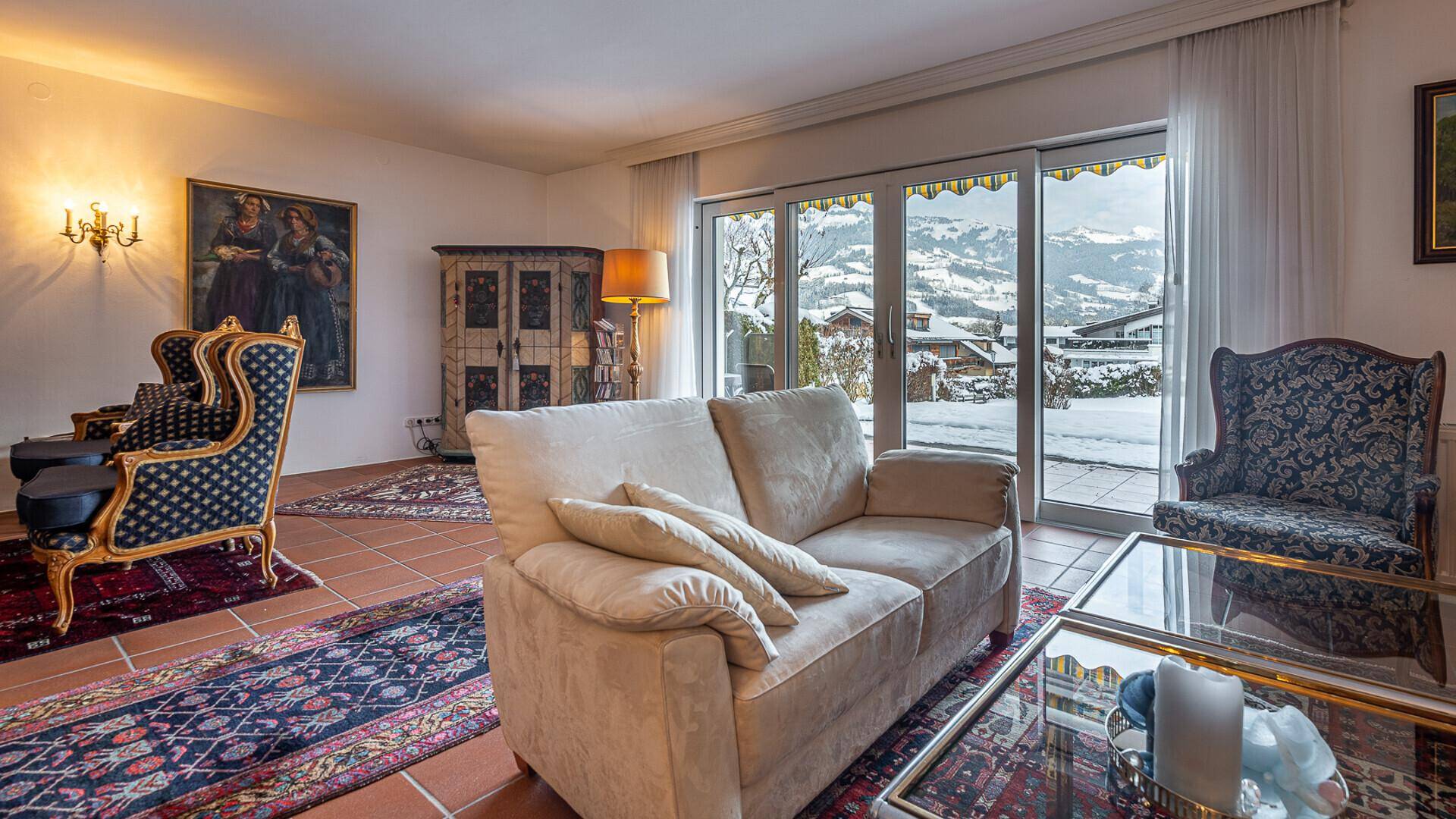 Gemütliches Wohnzimmer mit traditionellen Möbeln und großzügigem Blick auf die winterliche Berglandschaft.