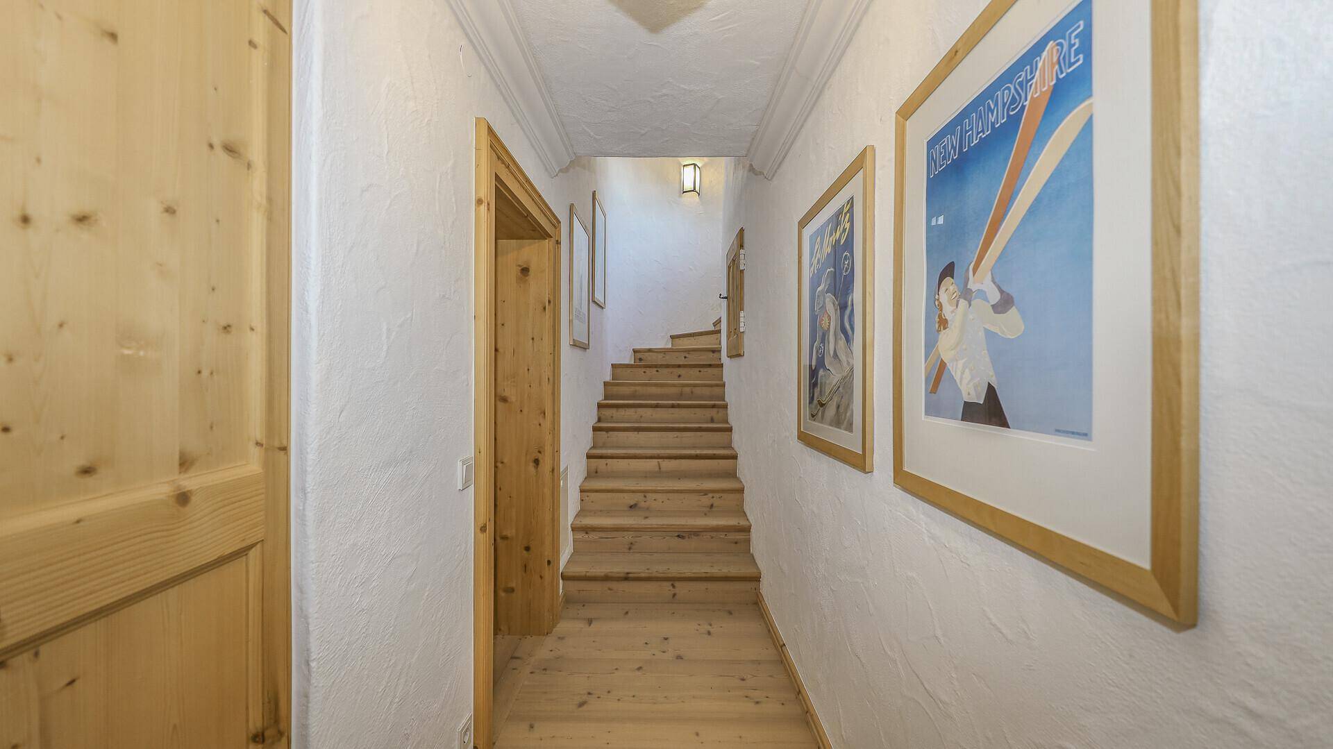 Langer Flur mit Holztreppe und gerahmten Bildern an den Wänden.