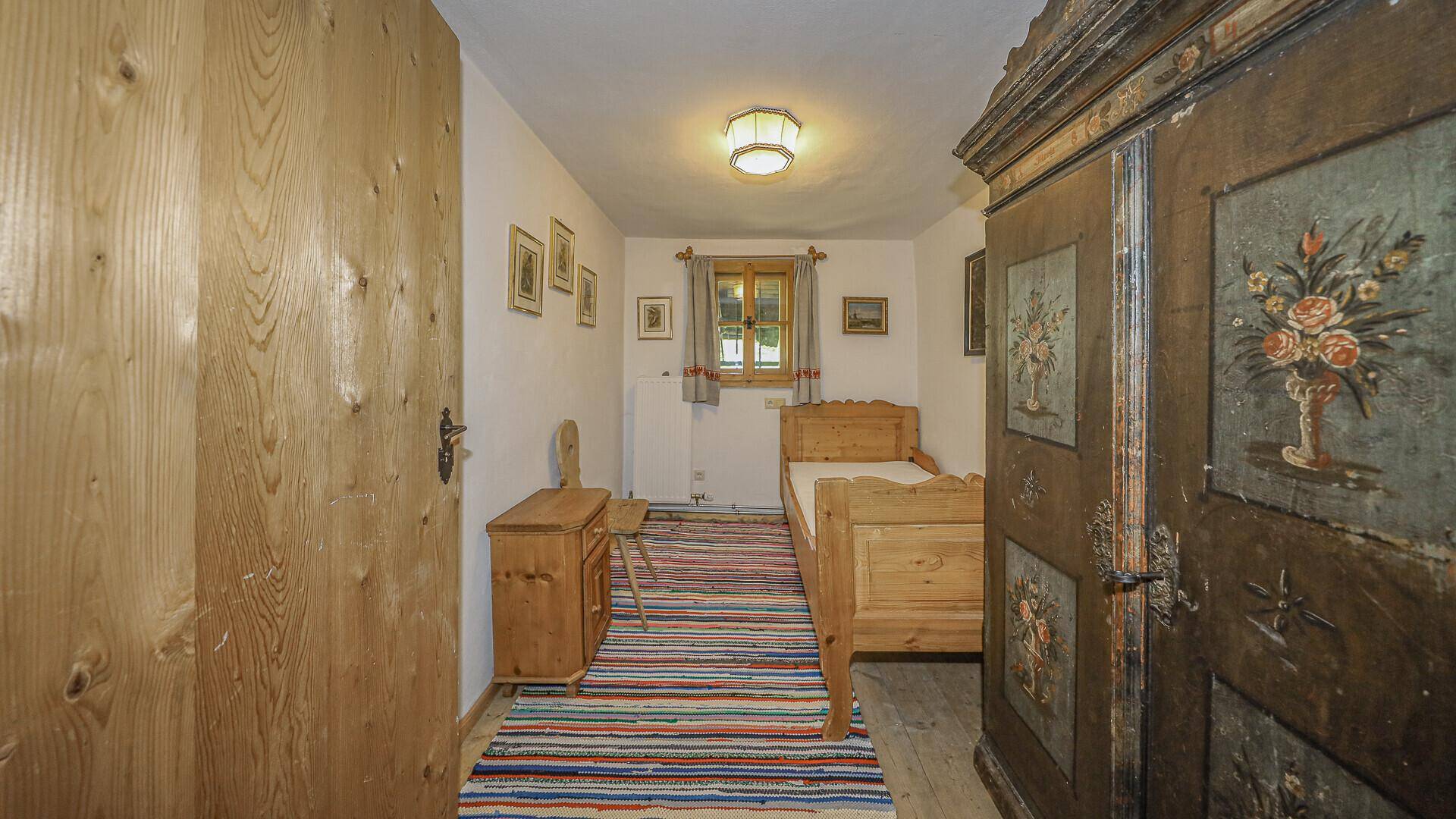 Kleines Schlafzimmer im Originalzustand mit Einzelbett, Holzmöbeln und bemaltem Kleiderschrank.