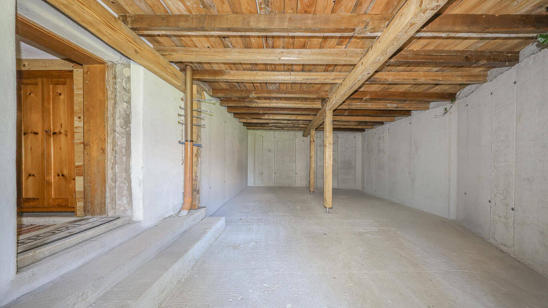 Unausgebauter Kellerraum mit sichtbarer Holzbalkendecke und Betonwänden, ideal als Stauraum.