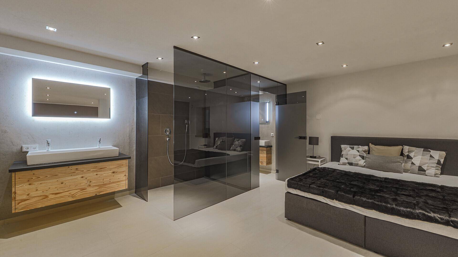 Offenes Schlafzimmer mit integriertem Badbereich, Doppelwaschbecken und Glasdusche.