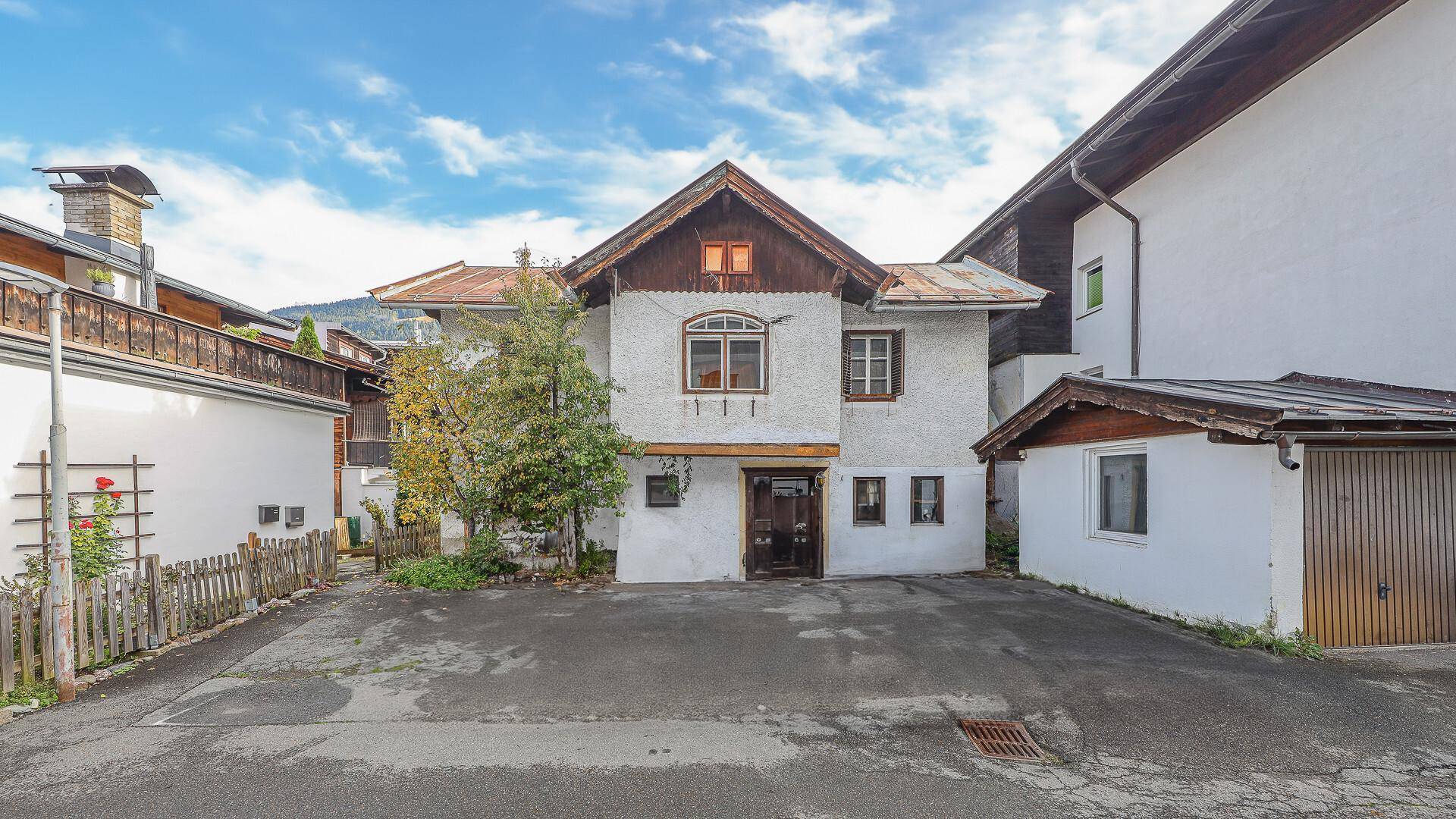 Vorderansicht eines renovierungsbedürftigen Hauses mit großem Vorplatz und Garage.