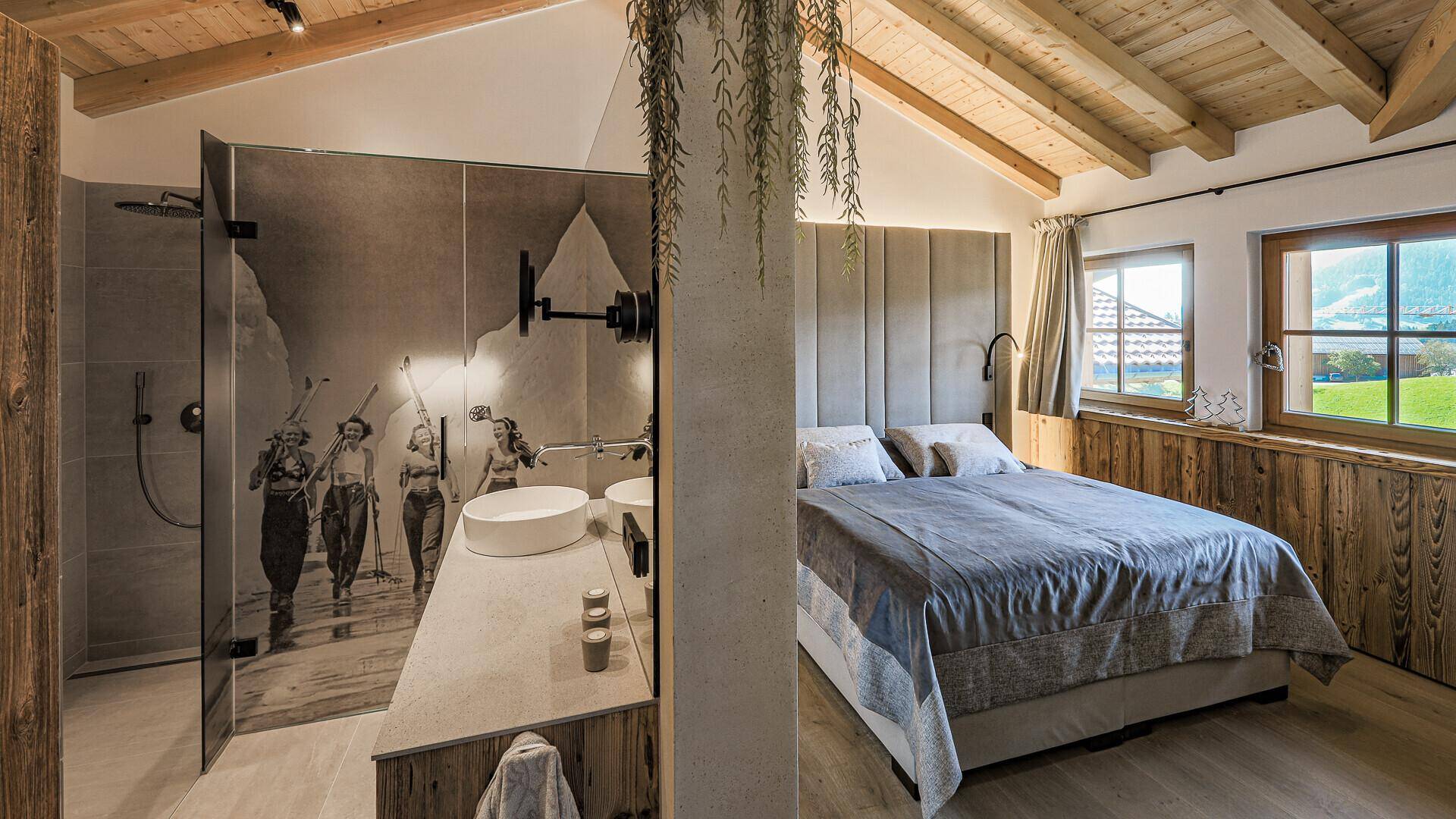 Schlafzimmer im alpinen Stil mit Holzwänden, Doppelbett und offenem Badezimmerbereich mit Dusche.