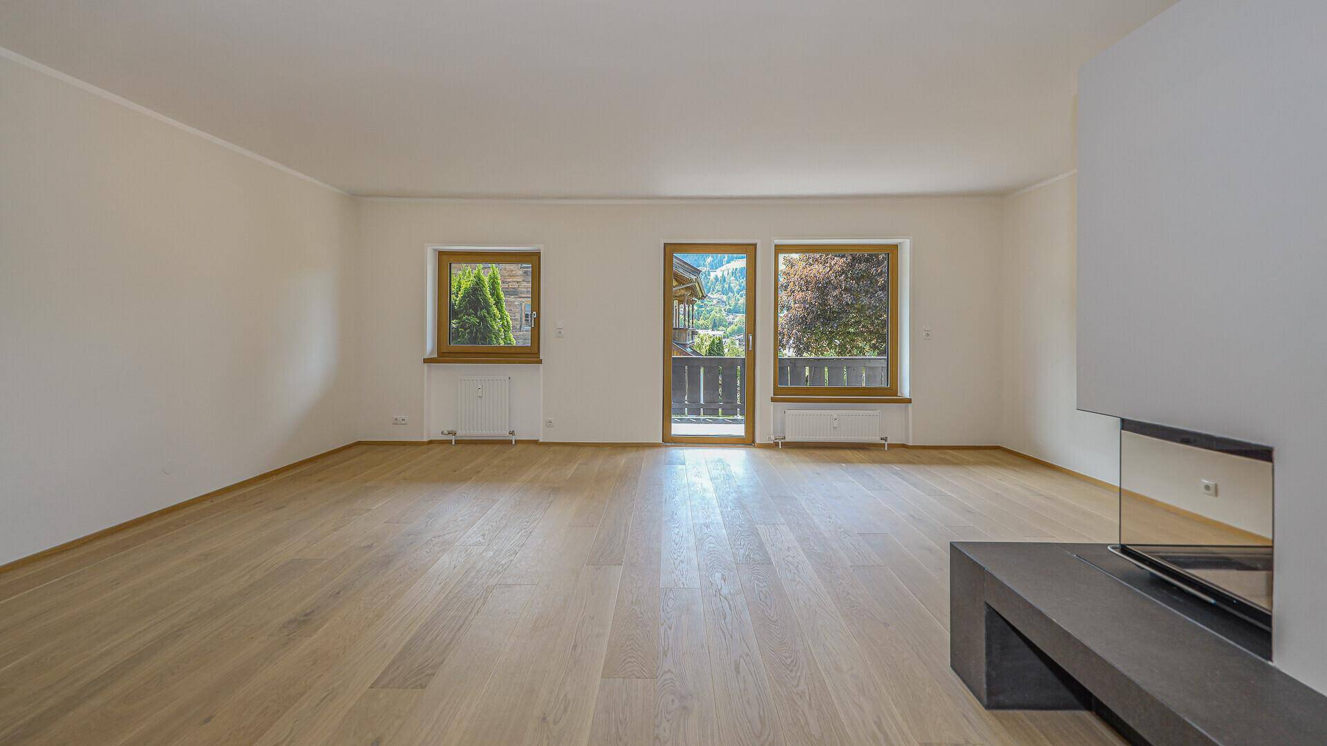 Heller, unmöblierter Raum mit Holzboden, Fenster und Balkonzugang, bietet Bergblick.