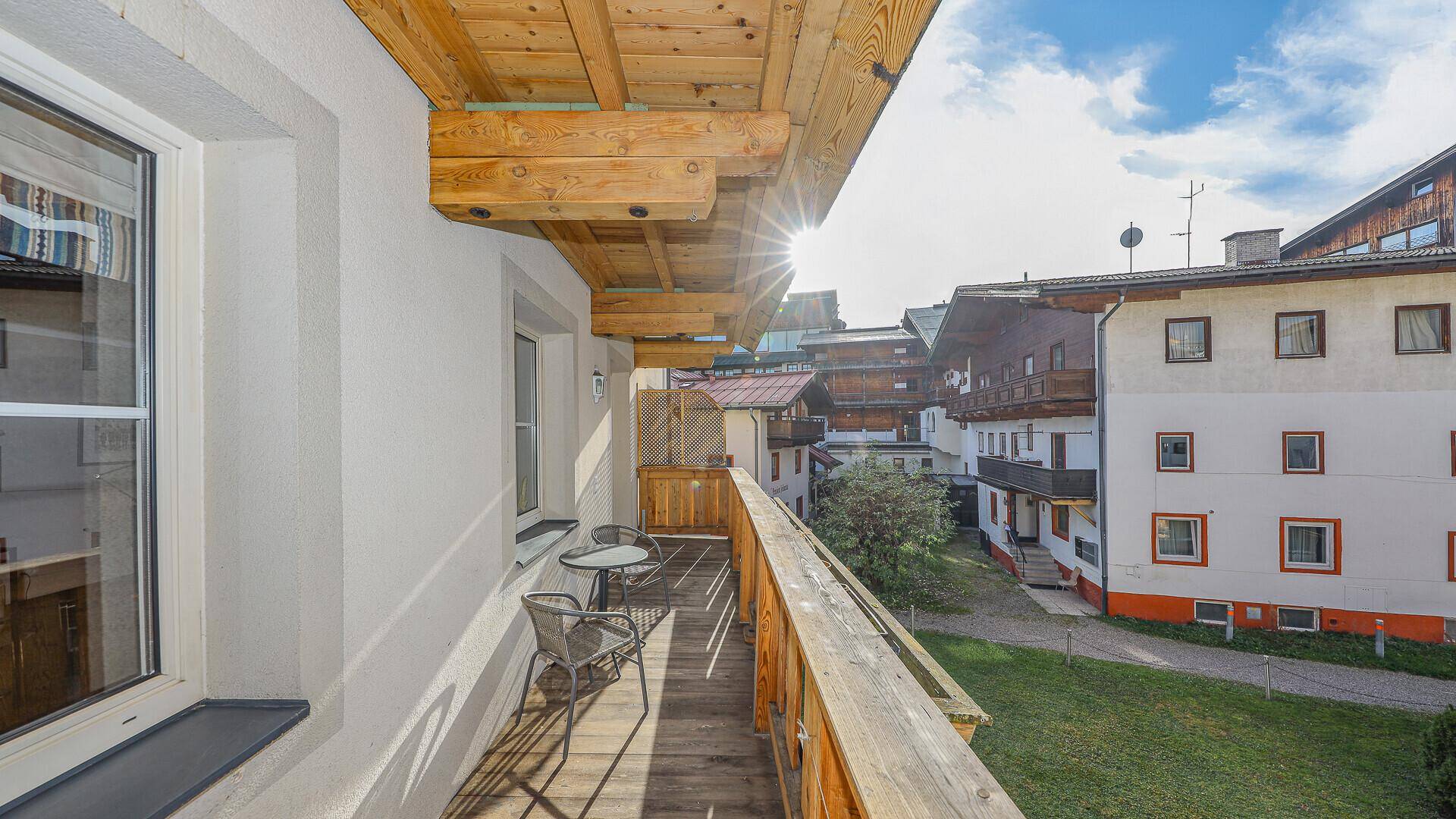Sonniger Holzbalkon mit Sitzgelegenheiten und Blick auf die umliegenden Gebäude und Grünflächen.