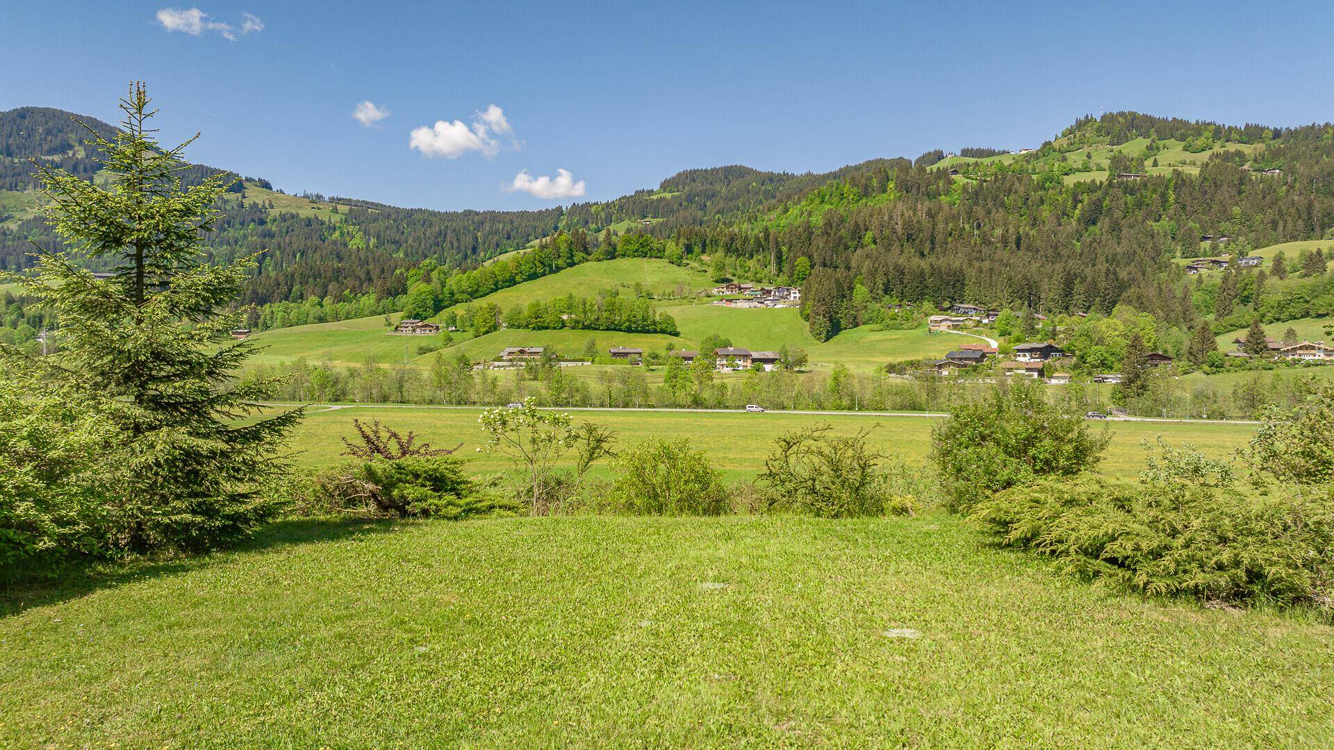 Weitläufige grüne Landschaft mit sanften Hügeln, Wäldern und traditionellen Häusern in der Ferne.