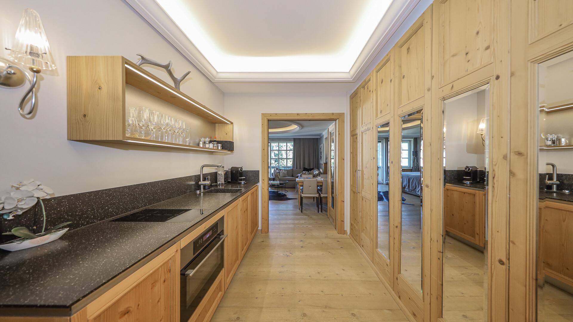 Moderne Küchenzeile mit Holzelementen, dunkler Arbeitsplatte und integrierten Geräten.