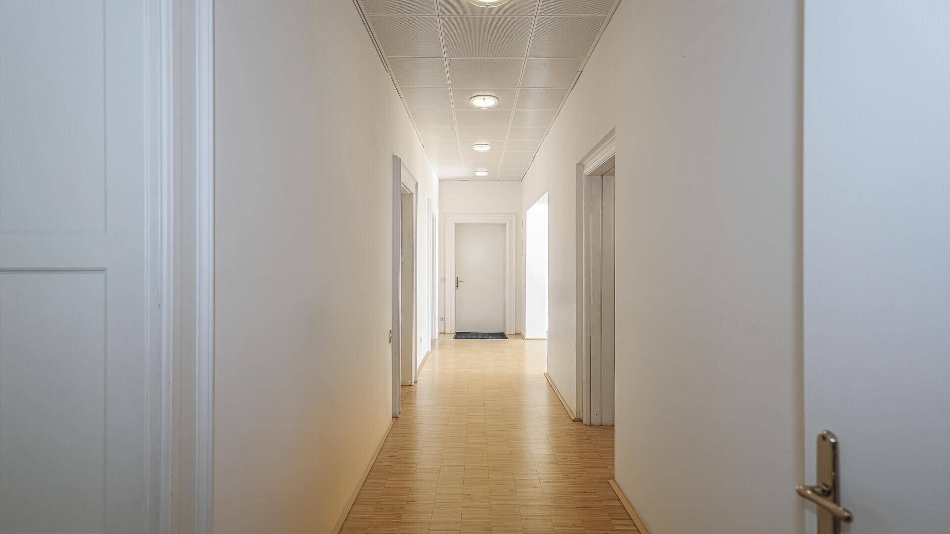 Heller, langer Flur mit Parkettboden und Einbaustrahlern in der Decke.