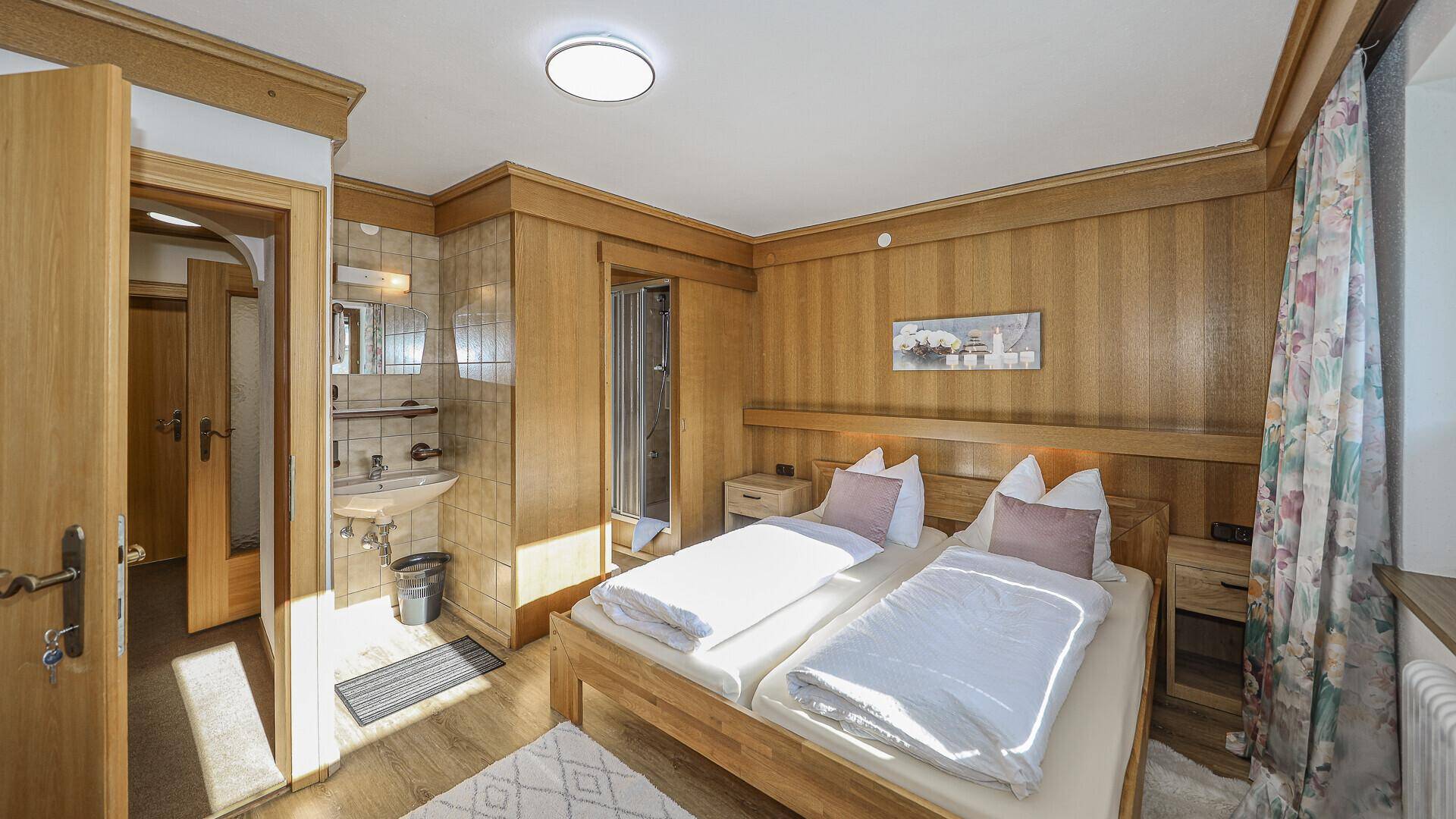 Gemütliches Schlafzimmer mit Holzvertäfelung, Doppelbett und integriertem Duschbereich.