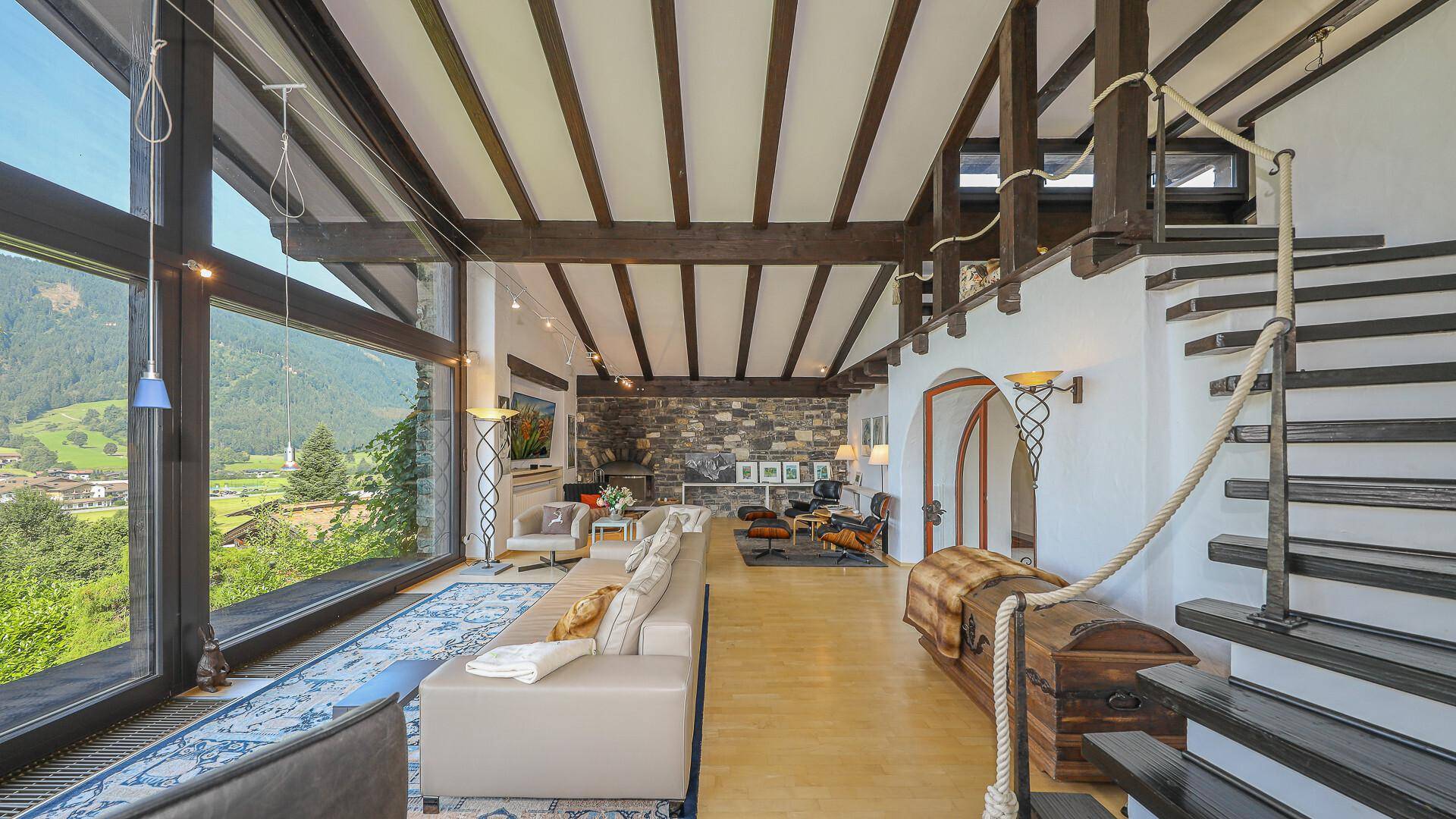 Offener Wohnbereich mit Holzbalkendecke, Steinelementen und einer Treppe zur Galerie.
