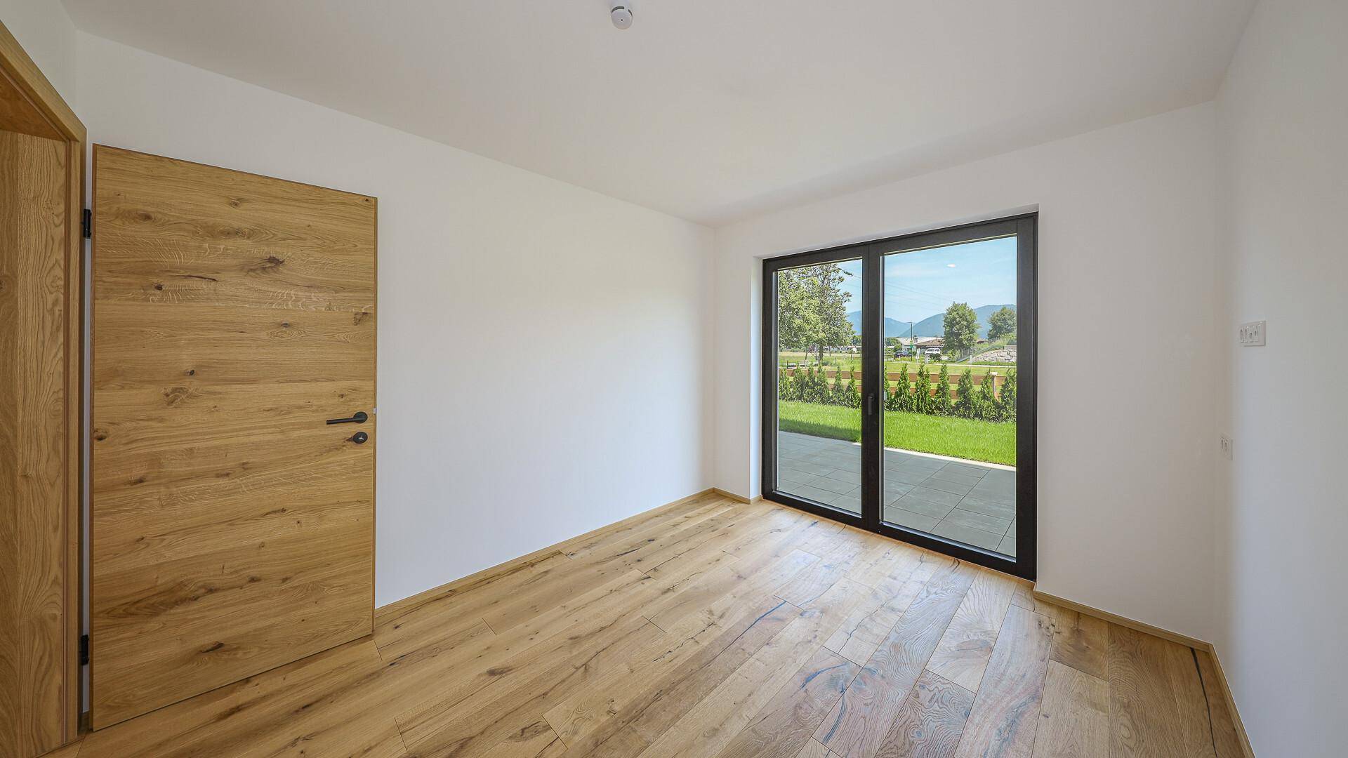Leeres Schlafzimmer mit Holzboden und großem Fenster, das viel Tageslicht hereinlässt.
