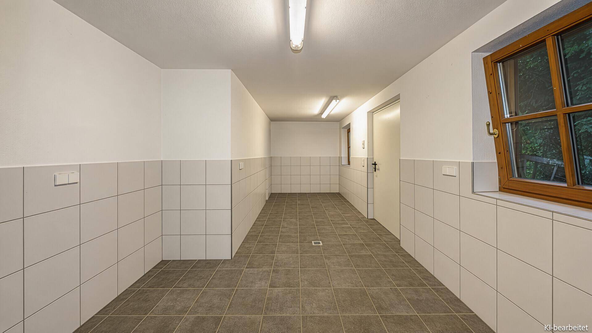 Funktionaler Raum mit halbhohen weißen Fliesen an den Wänden und grauen Bodenfliesen.