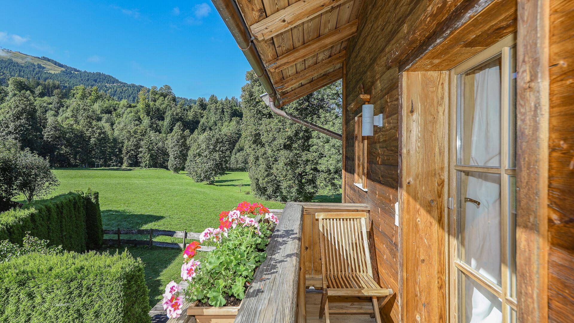 Kleiner Holzbalkon mit Blumenkästen und weitem Blick über grüne Wiesen und Berge.