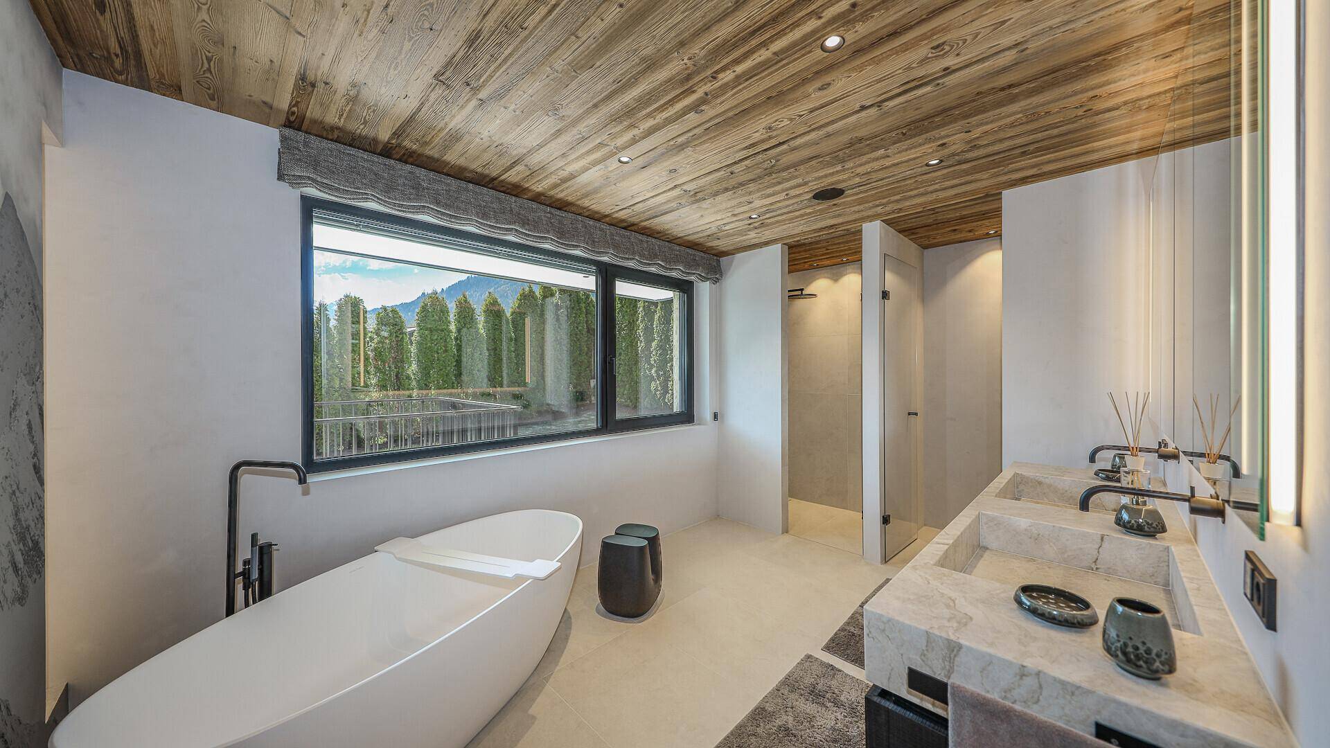 Luxuriöses Badezimmer mit freistehender Badewanne, Doppelwaschbecken und Panoramafenster mit Bergblick.