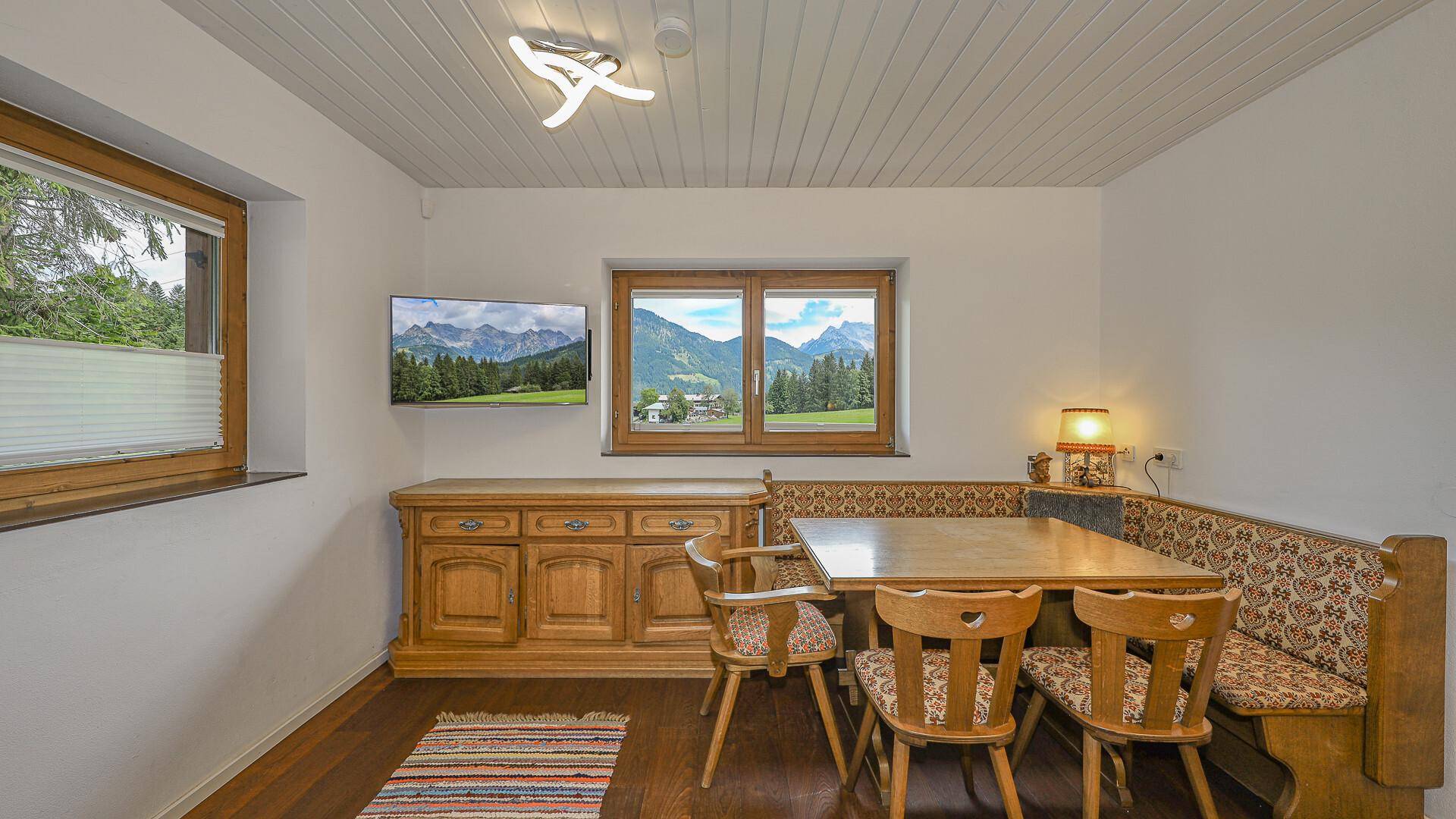 Rustikaler Essbereich mit Holztisch, Eckbank und Bergblick durch das Fenster.