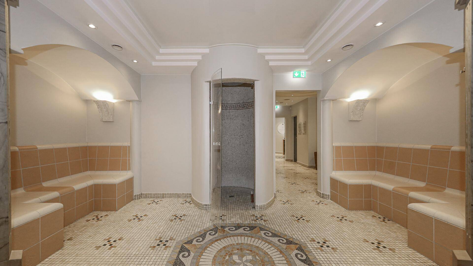Wellnessbereich mit Dampfbad-Bänken, Dusche und dekorativen Fliesen.