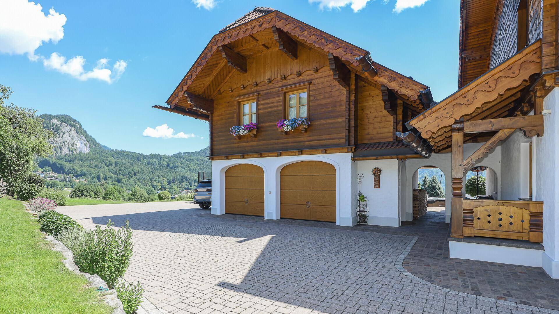 Traditionelles Haus mit Holzfassade, Doppelgarage und gepflasterter Auffahrt in alpiner Umgebung.