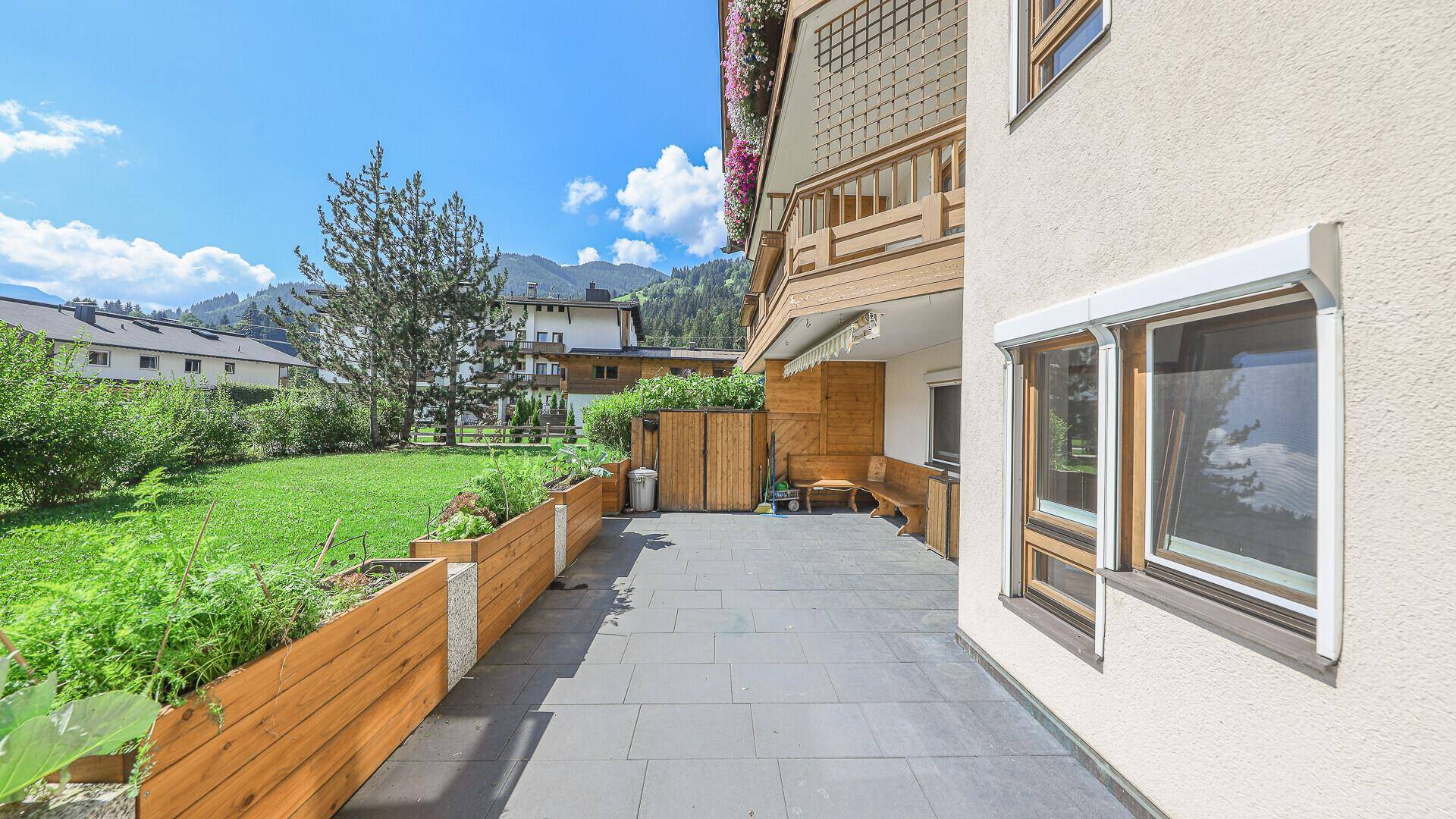 Große Terrasse mit Gartenbeeten, Rasenfläche und weitem Blick auf die umliegende Bergwelt.