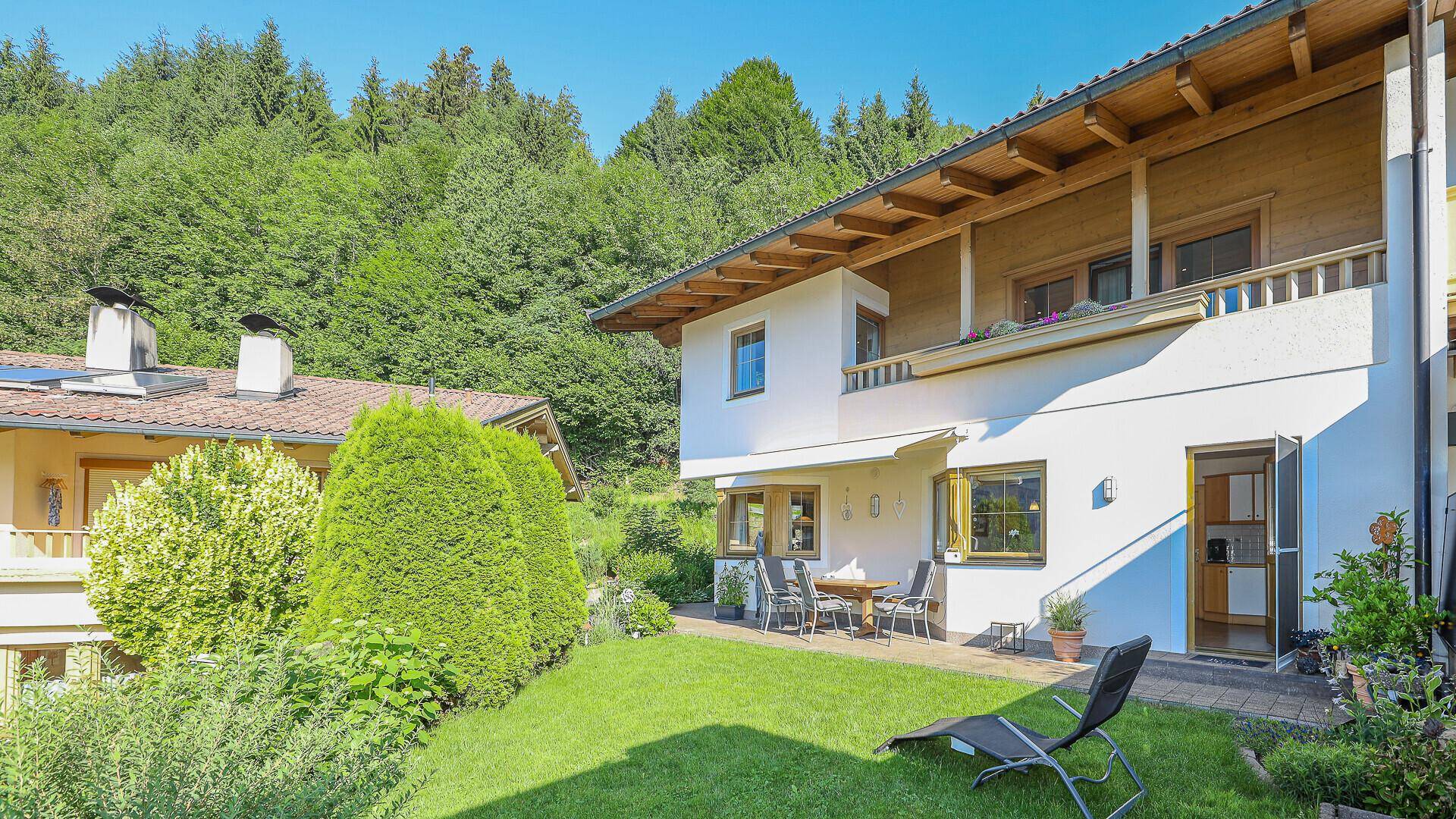 Gepflegter Gartenbereich mit Terrasse, Liegestuhl und Blick auf die umliegende Berglandschaft.