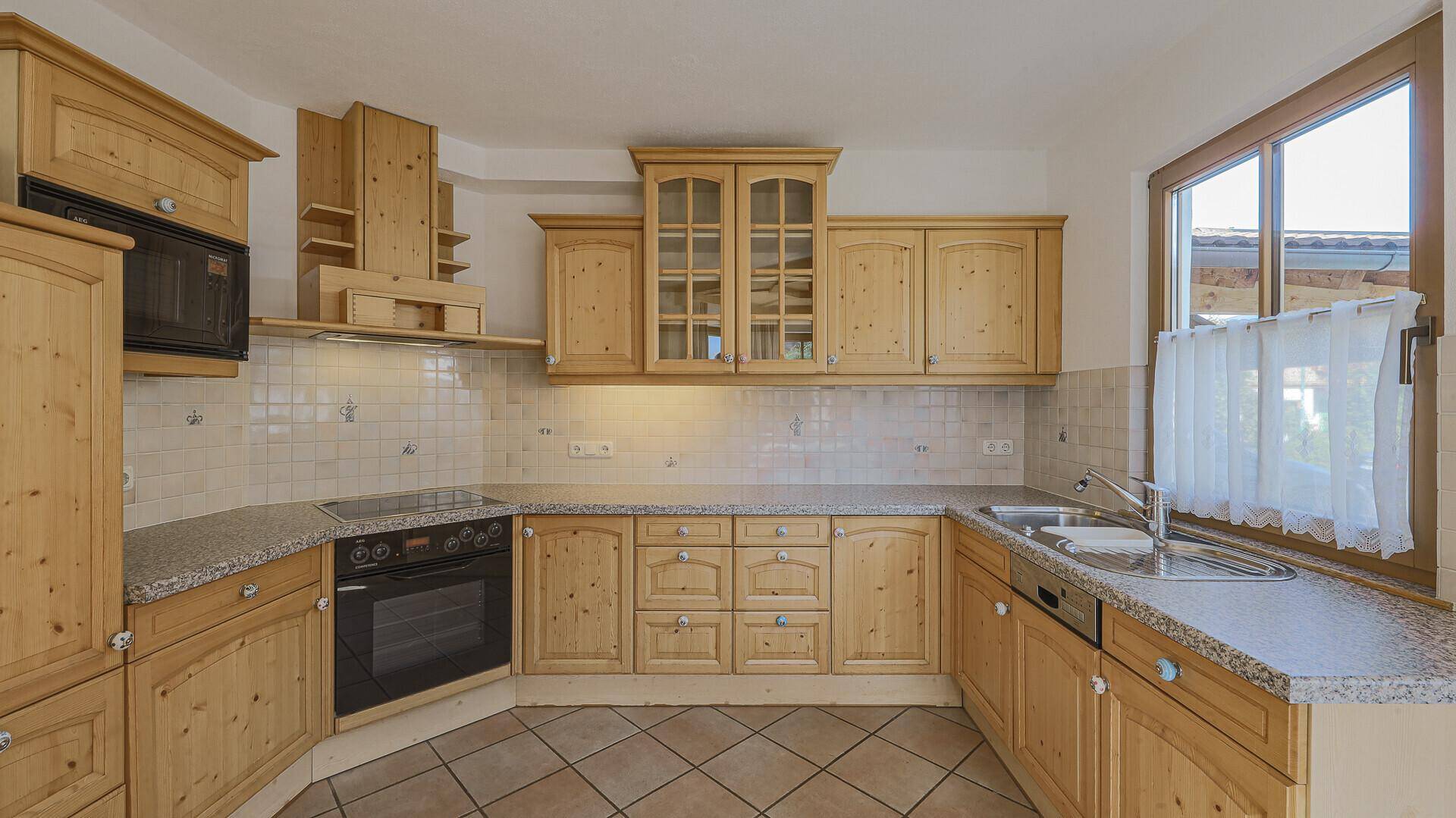 Traditionelle Holzküche mit Fliesenrückwand, Einbaugeräten und Fenster.