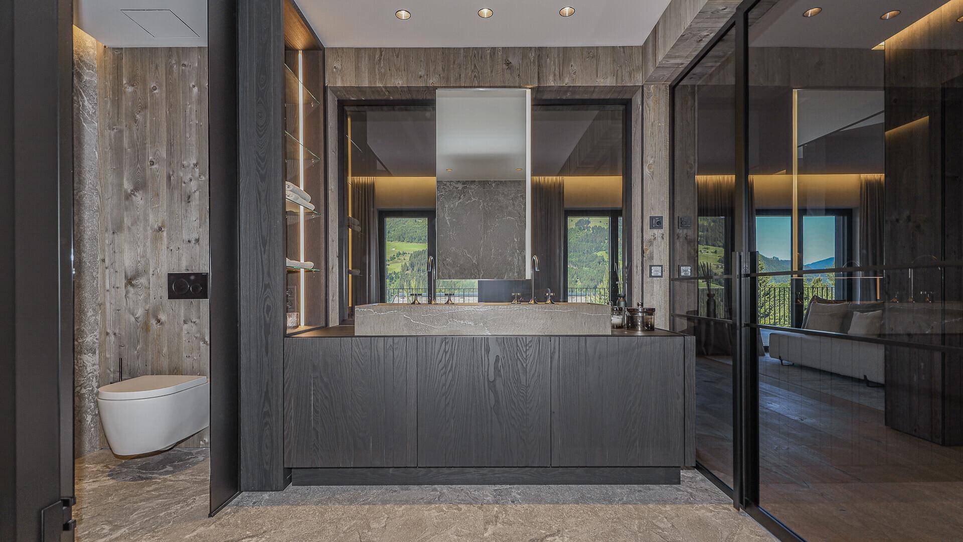 Modernes Badezimmer mit dunklen Holzmöbeln, Steinwaschbecken und separatem WC-Bereich.