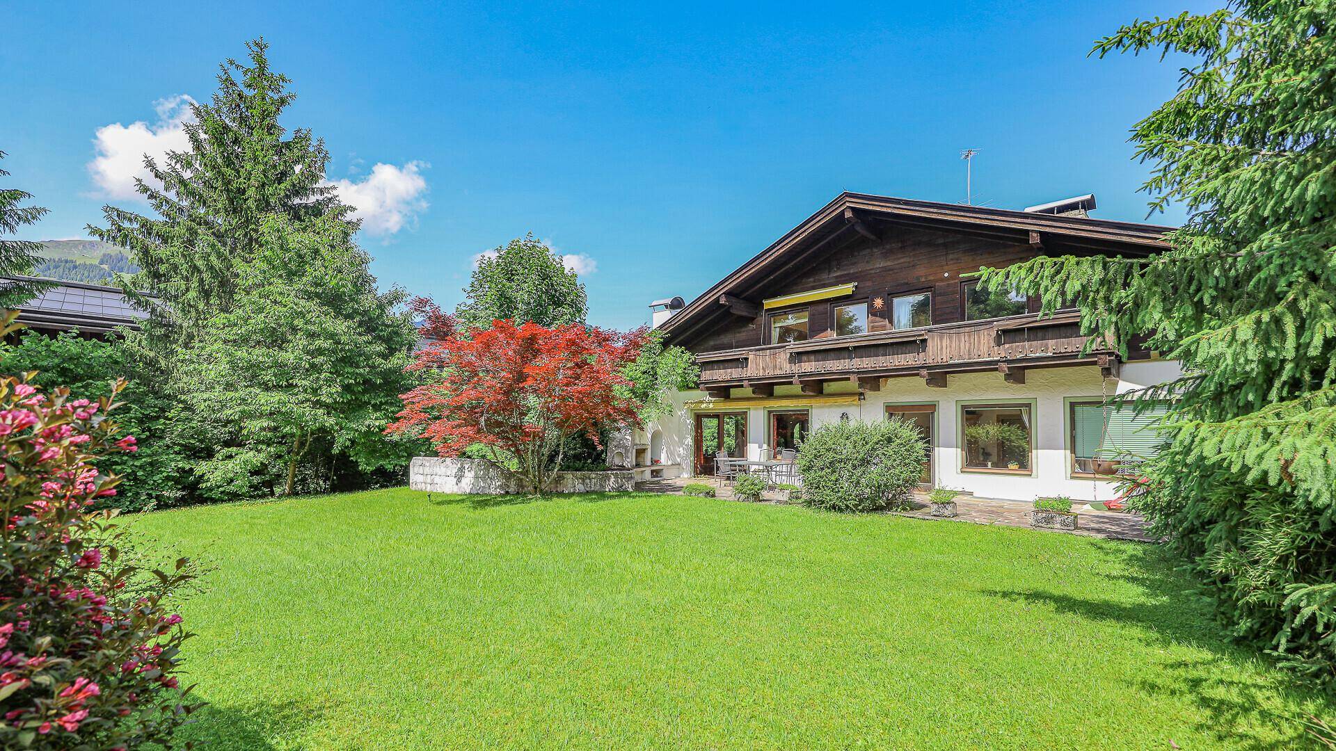 Großer, gepflegter Garten mit Rasenfläche, rotem Ahornbaum und dem Chalet im Hintergrund.