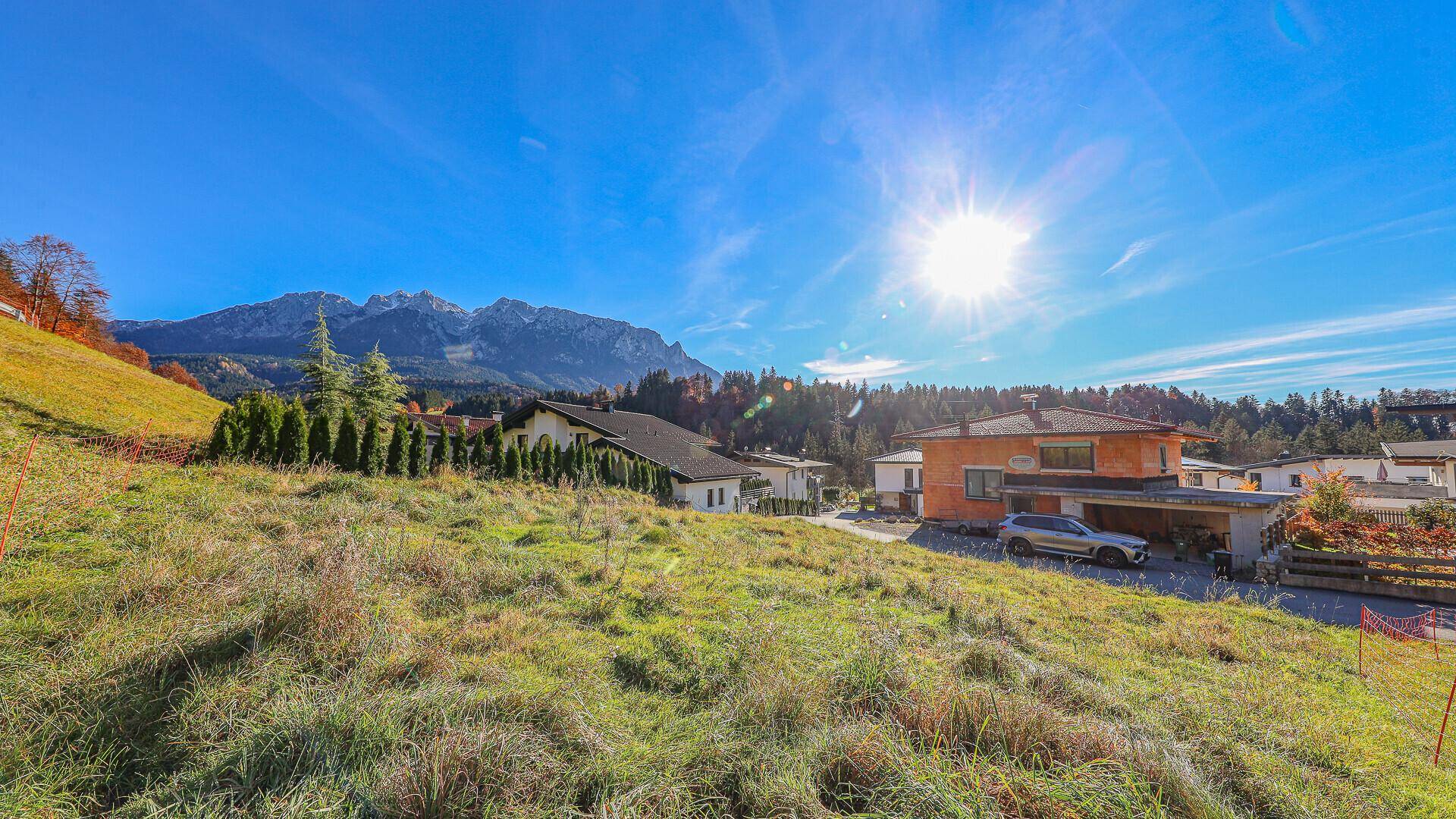 Sonnige Landschaft mit grünen Wiesen, Häusern und majestätischen Bergen im Hintergrund.