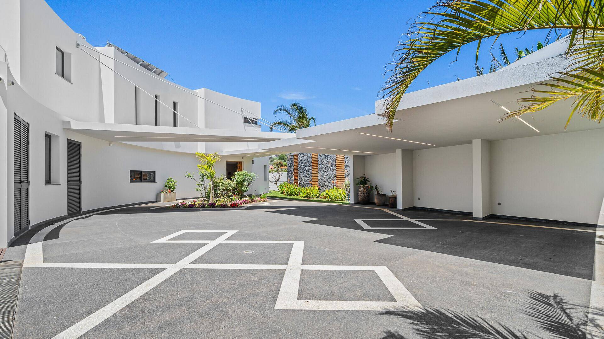 Moderne Zufahrt mit Carport und der weißen, geschwungenen Architektur des Gebäudes.