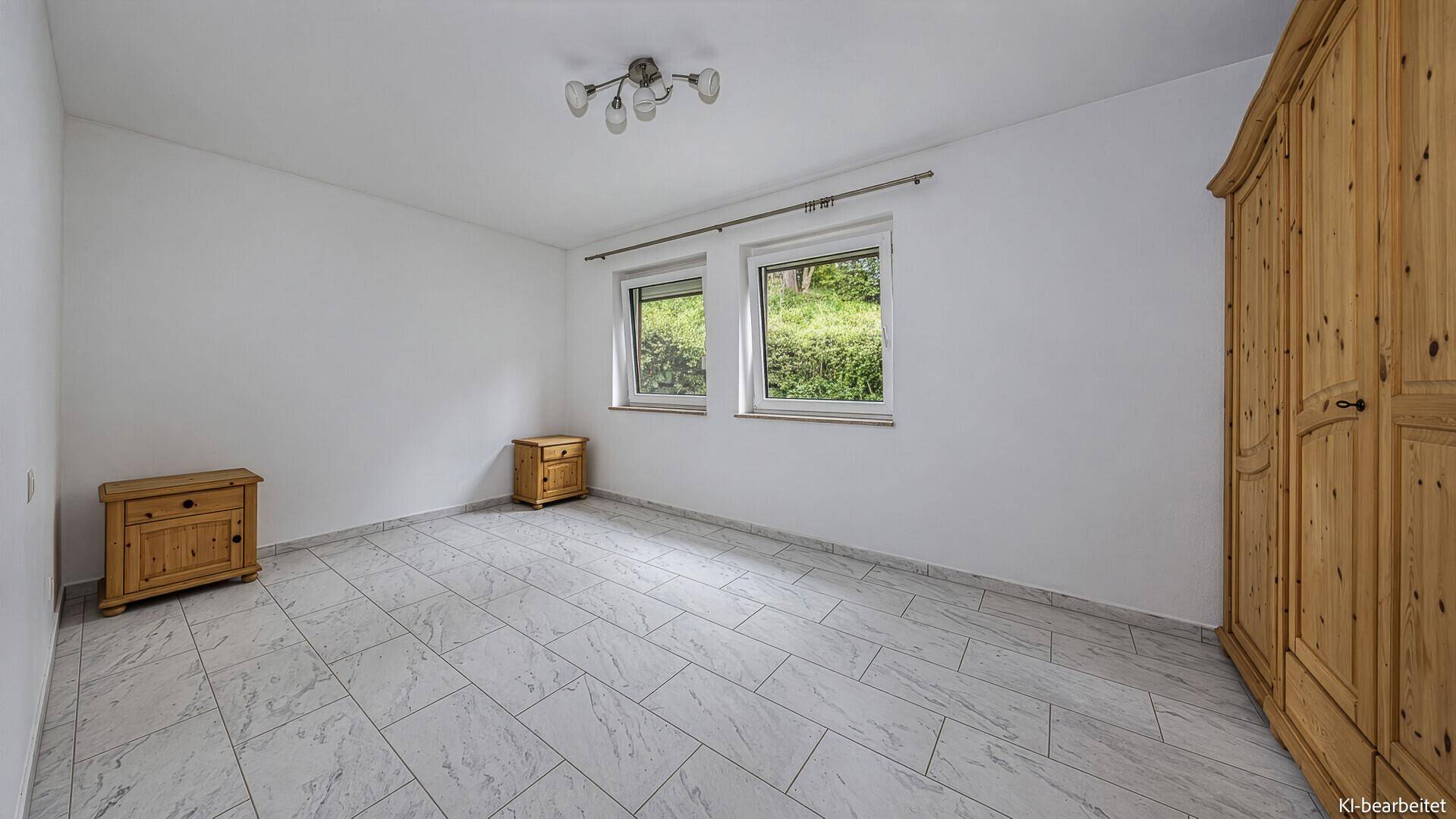 Geräumiges Schlafzimmer mit Fliesenboden, Holzschrank und zwei Fenstern mit Blick ins Grüne.
