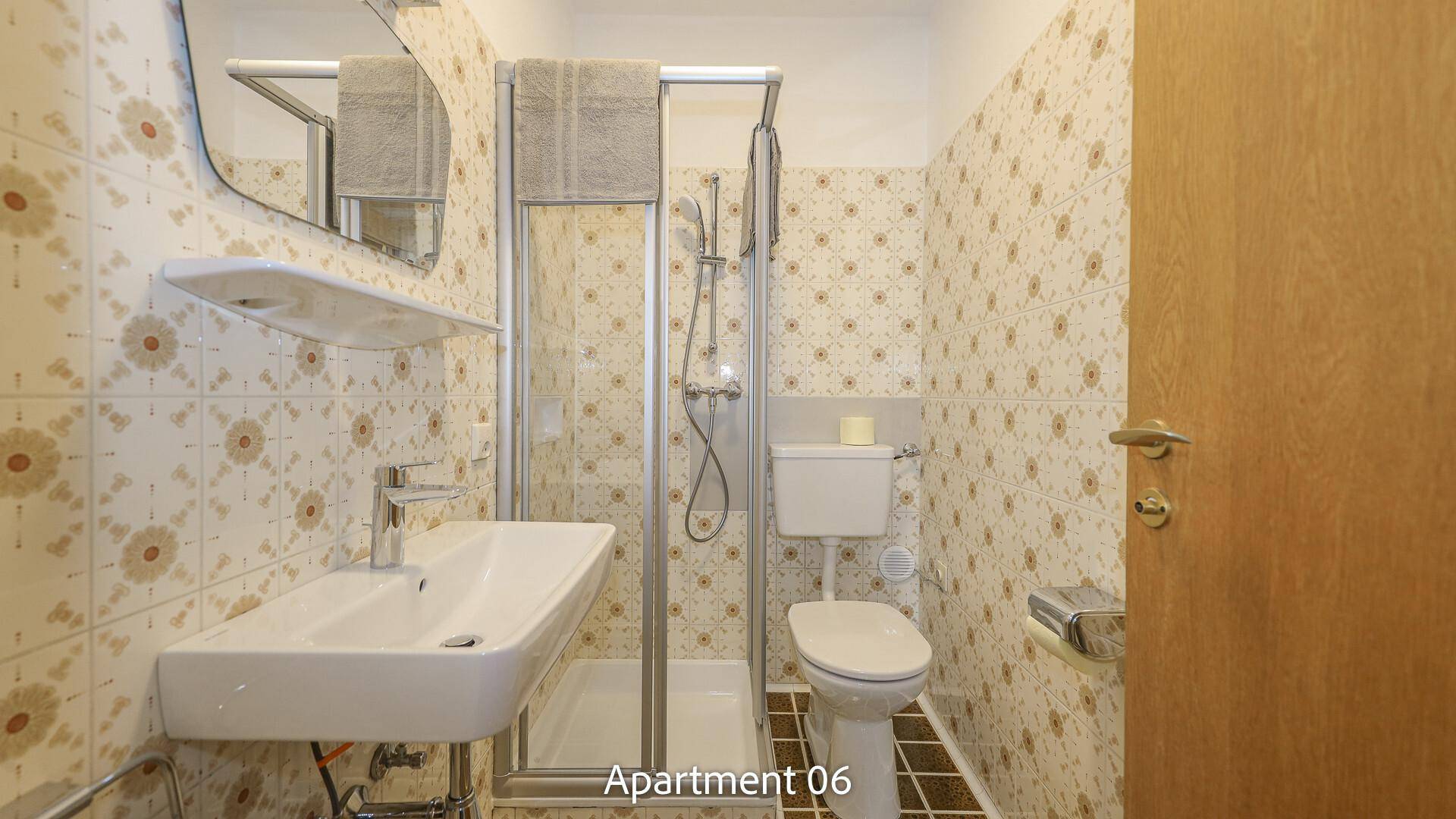 Badezimmer von Apartment 06 mit gemusterten Fliesen, Waschbecken, WC und einer Duschkabine.