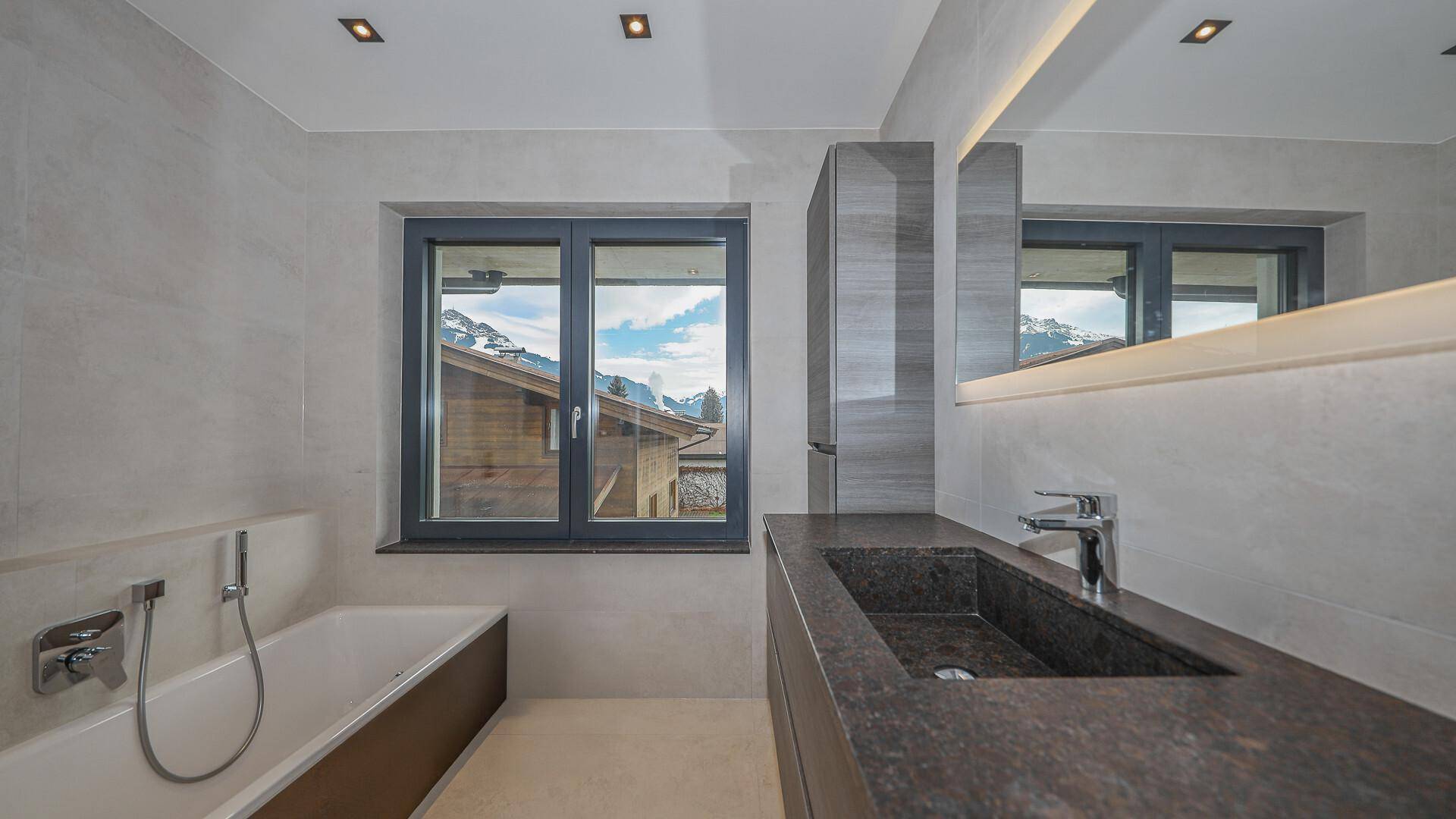 Modernes Badezimmer mit Badewanne, dunklem Waschbecken und Fenster mit Bergblick.