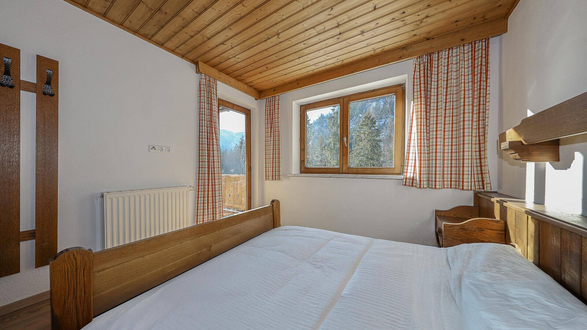 Gemütliches Schlafzimmer mit Holzbett, Holzdecke und Fenster mit Bergblick.