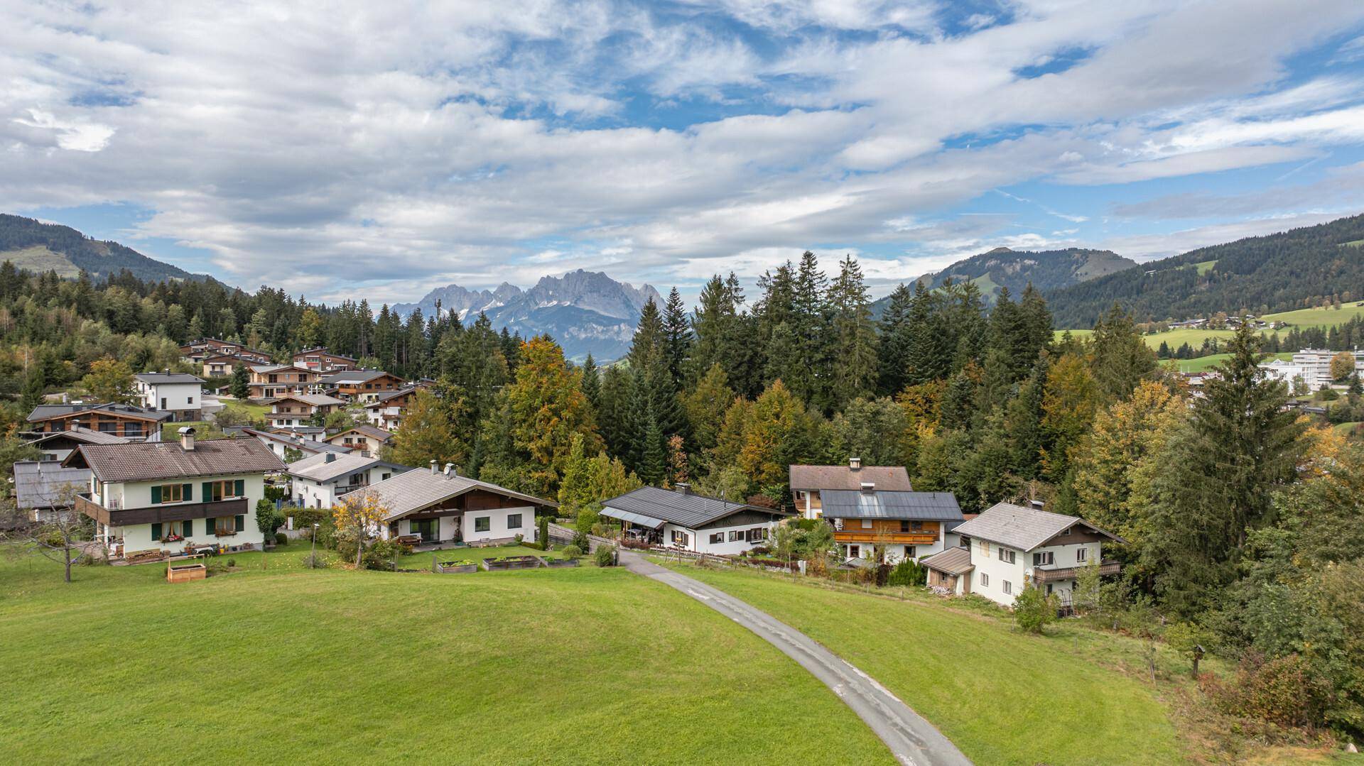 Weitwinkelaufnahme einer malerischen Wohnsiedlung, eingebettet in eine grüne Berglandschaft unter bewölktem Himmel.