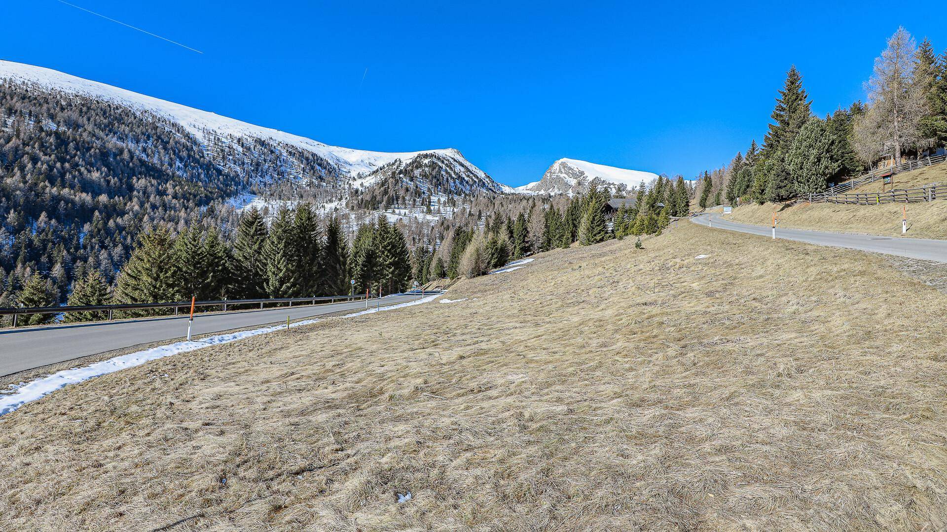 Sonniger Hang mit einer Straße und Blick auf die schneebedeckten Berge in der Ferne.