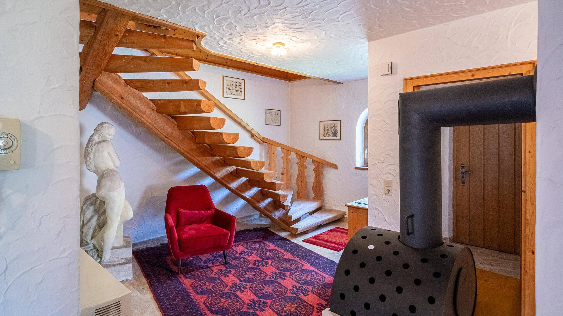 Heller Flur mit Holztreppe, rotem Sessel und dekorativer Statue, mit Blick auf den Ofen.