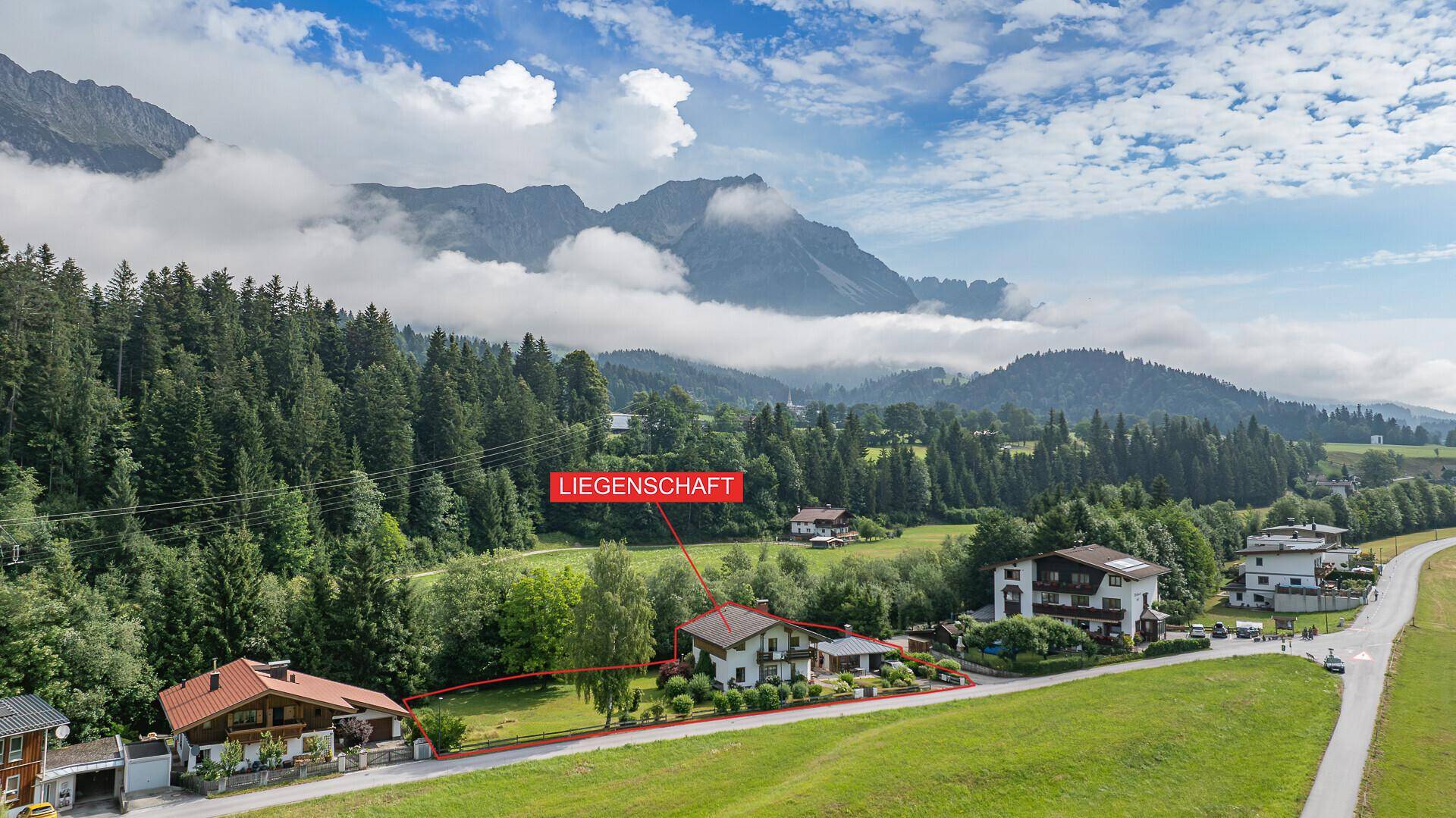 Luftaufnahme eines Hauses mit Garten in einer malerischen Berglandschaft, umgeben von viel Grün.