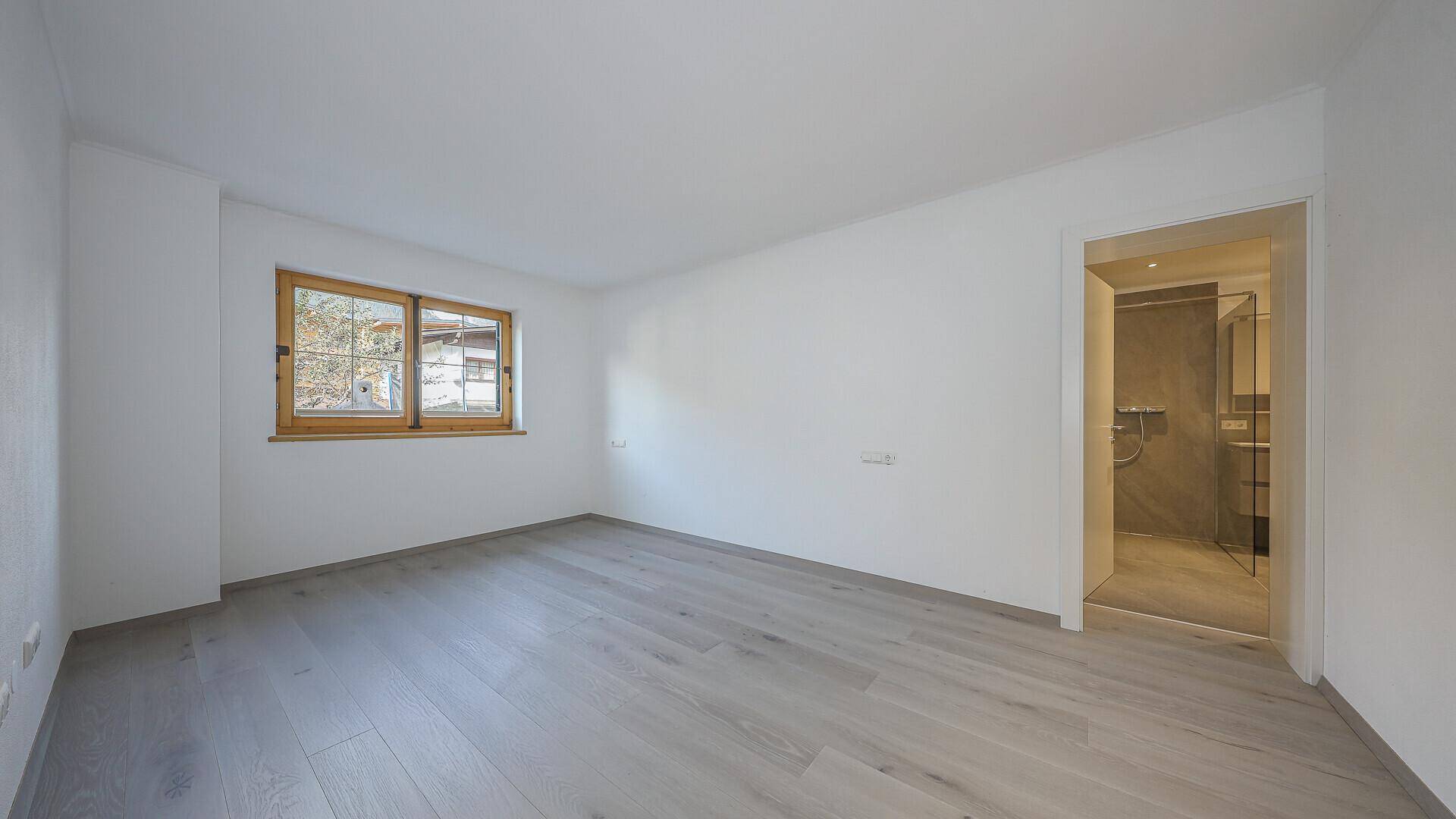Helles, leeres Schlafzimmer mit Holzboden und direktem Zugang zu einem modernen Badezimmer.