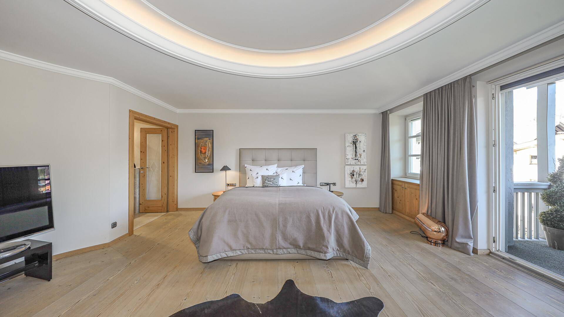 Schlafbereich mit großem Bett, Holzboden und direktem Zugang zum Balkon.