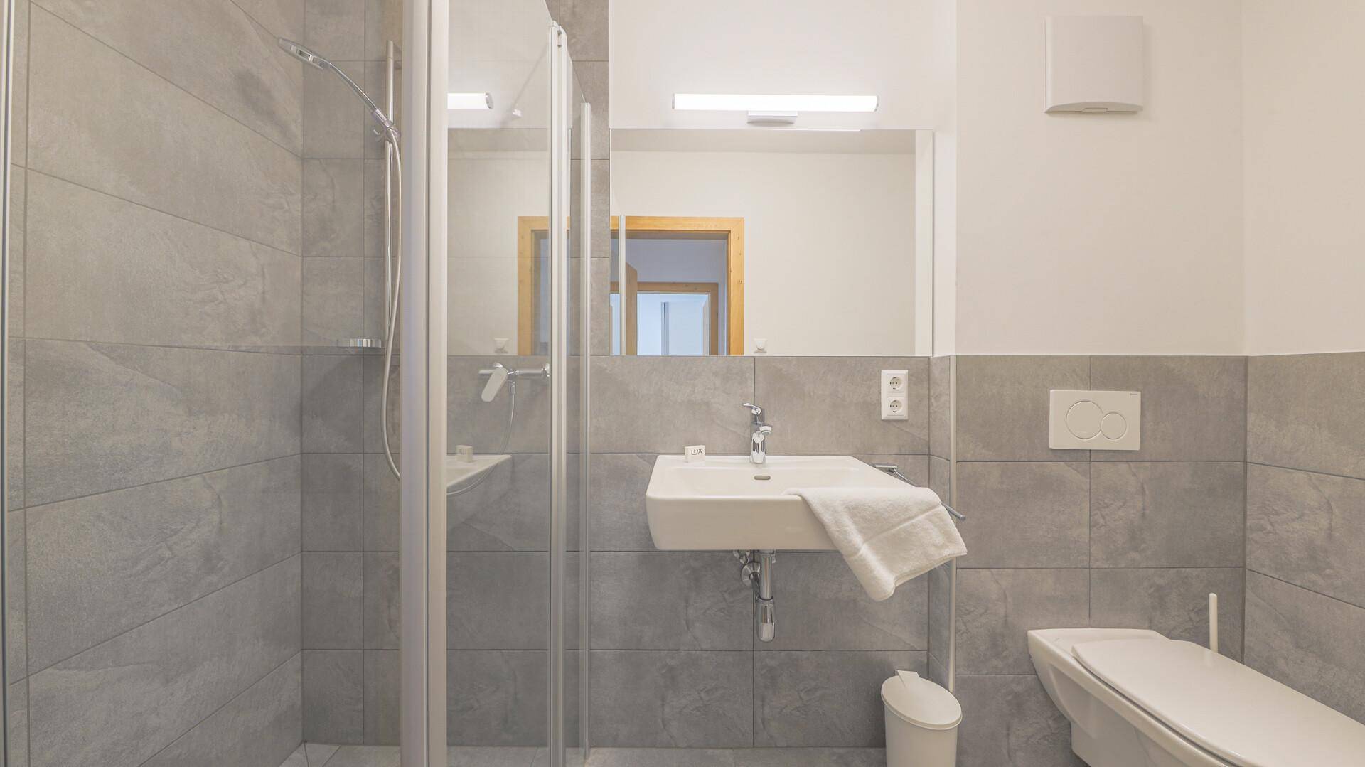 Modernes Badezimmer mit grauen Fliesen, ebenerdiger Dusche und wandhängendem WC.