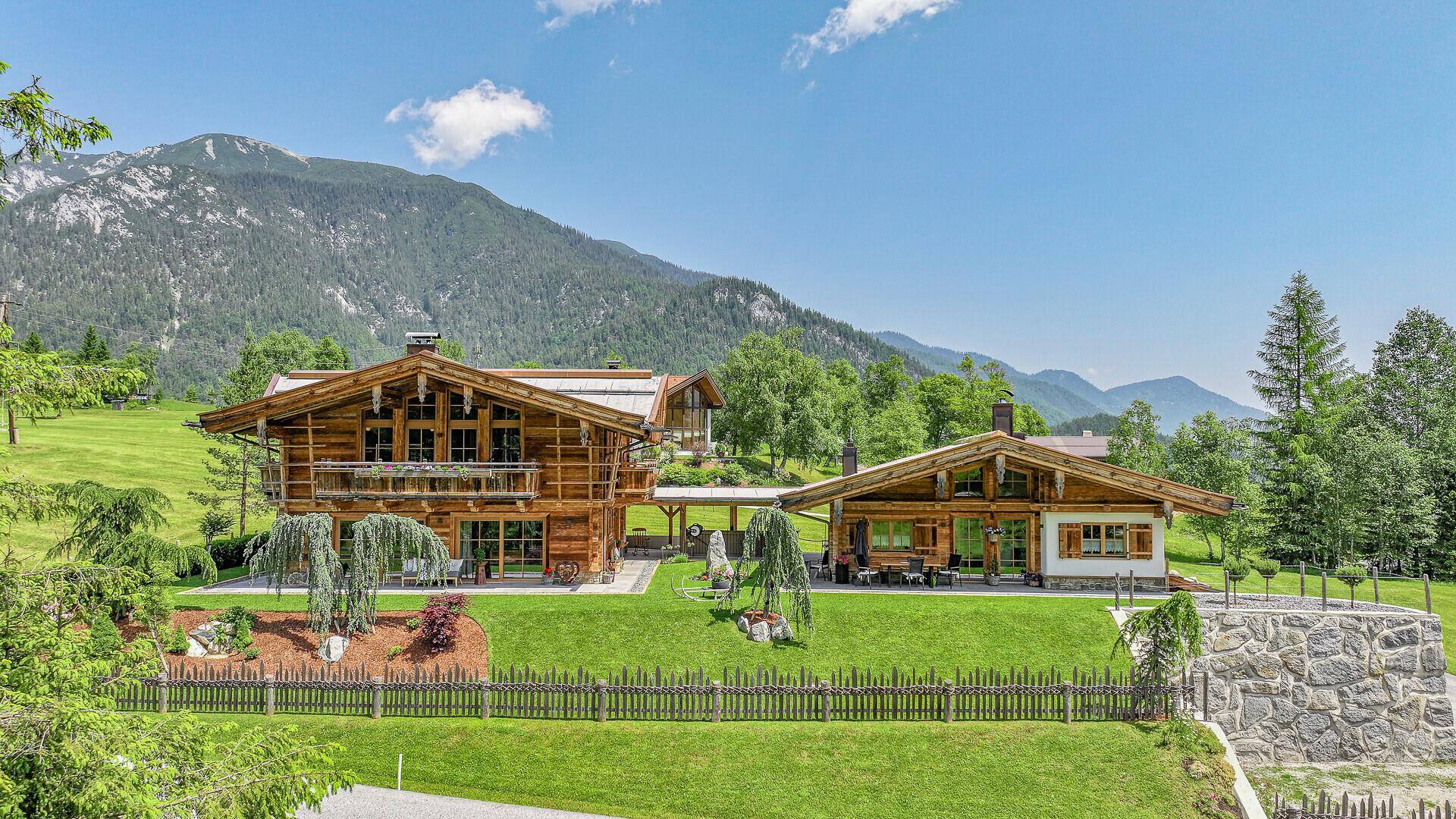 Zwei charmante Chalets mit Holzbalkonen und grünen Gärten, umgeben von einer malerischen Berglandschaft.